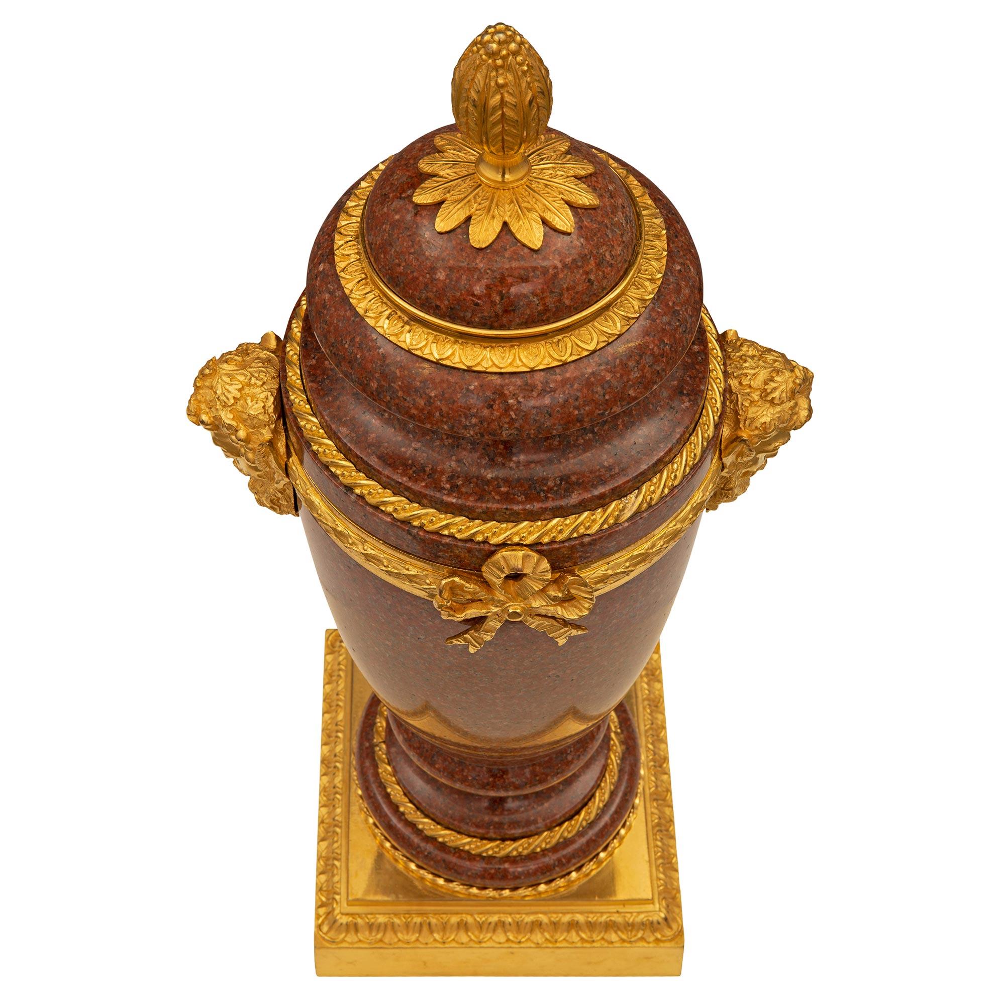 A superb pair of French 19th century Louis XVI st. ormolu and red granite urns. Each urn is raised by an elegant square base with a fine mottled border and a wrap around palmette designed band. The mottled granite socle shaped pedestal supports are