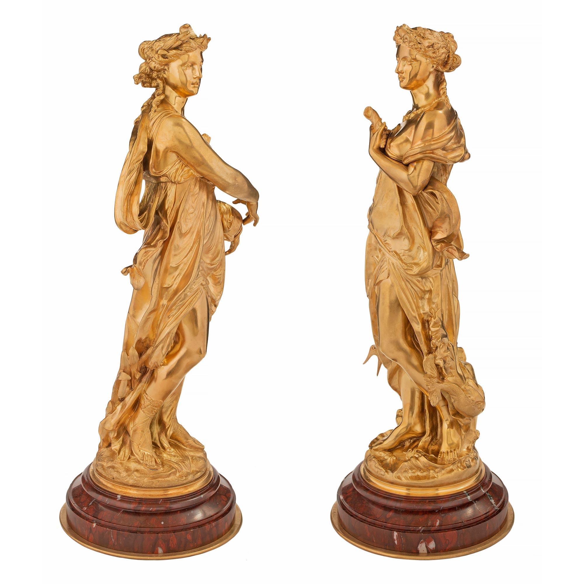 A striking true pair of French 19th century Louis XVI st. Belle Époque period ormolu and rouge Griotte statues. Each statue is raised by a circular rouge Griotte base with a fine bottom ormolu band and a mottled design. The statues are of beautiful