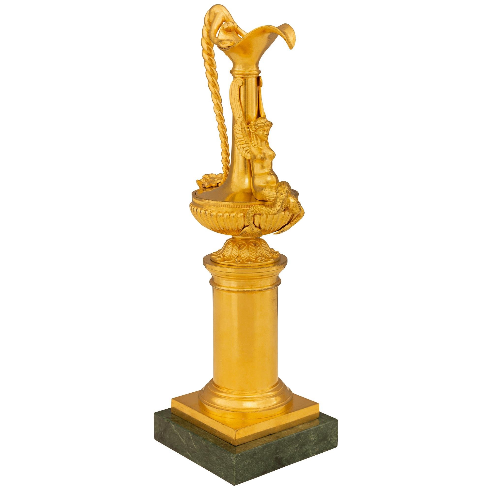 Paire d'aiguières très décoratives en bronze doré et marbre Verde Indio de style Louis XVI du XIXe siècle. Chaque aiguière de petite taille est surmontée d'une base carrée en marbre Verde Indio, au-dessous d'une colonne centrale à l'élégant motif