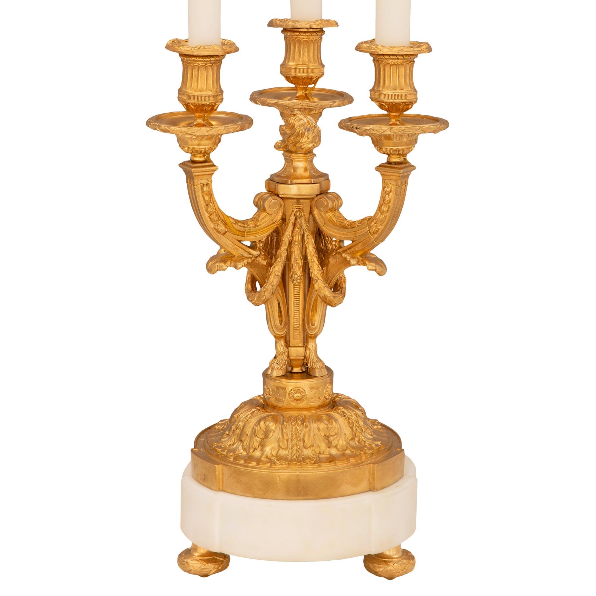 A beautiful and high quality pair of French 19th century Louis XVI st. ormolu and white Carrara marble lamps. Each three arm candelabra lamp is raised by a circular white Carrara marble base with elegant topie shaped ormolu feet with a fine wrap