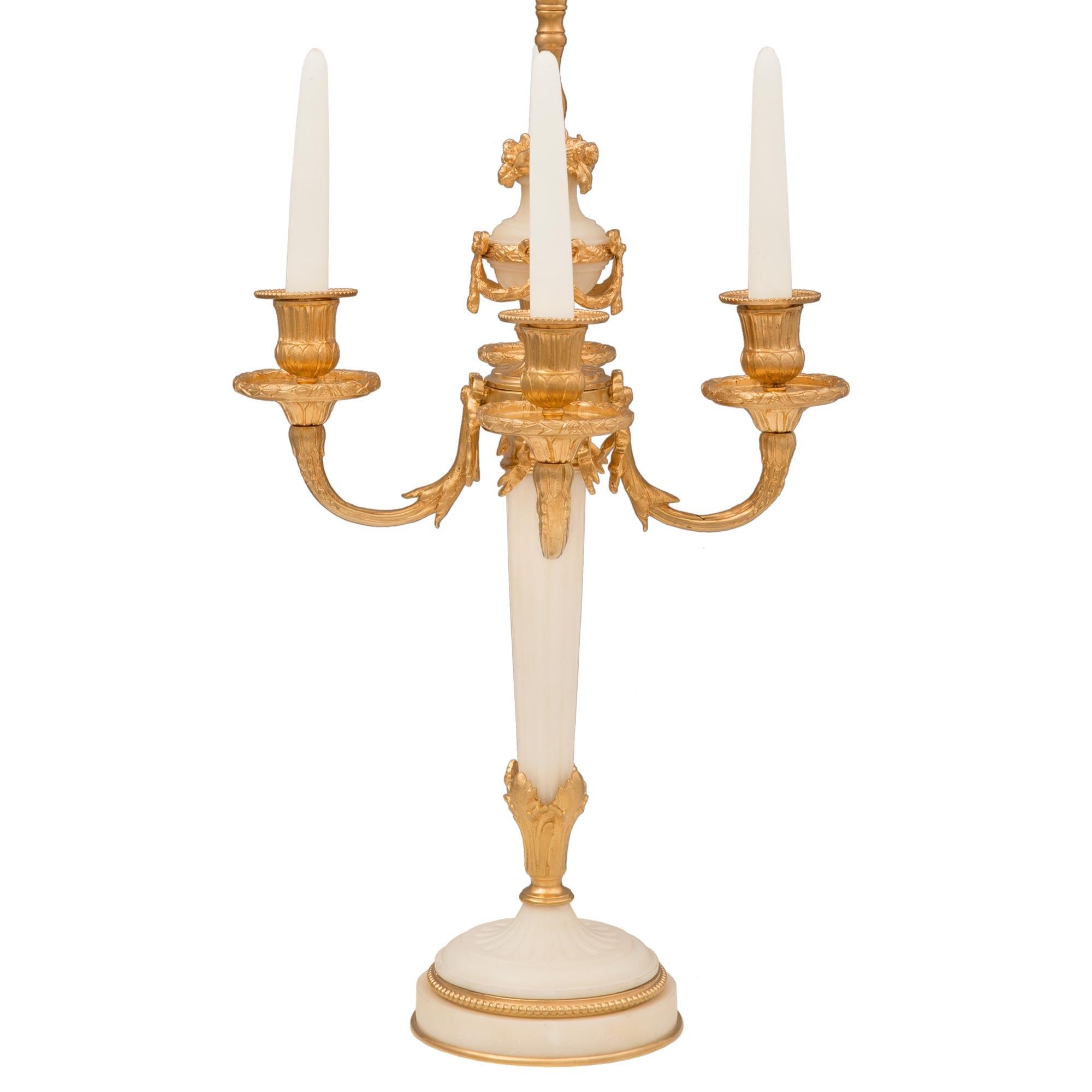 An extremely elegant and high quality pair of French 19th century Louis XVI st. ormolu and white Carrara marble lamps. Each four arm lamp is raised by a circular white Carrara marble base with a fine bottom ormolu fillet, a lovely wrap around beaded