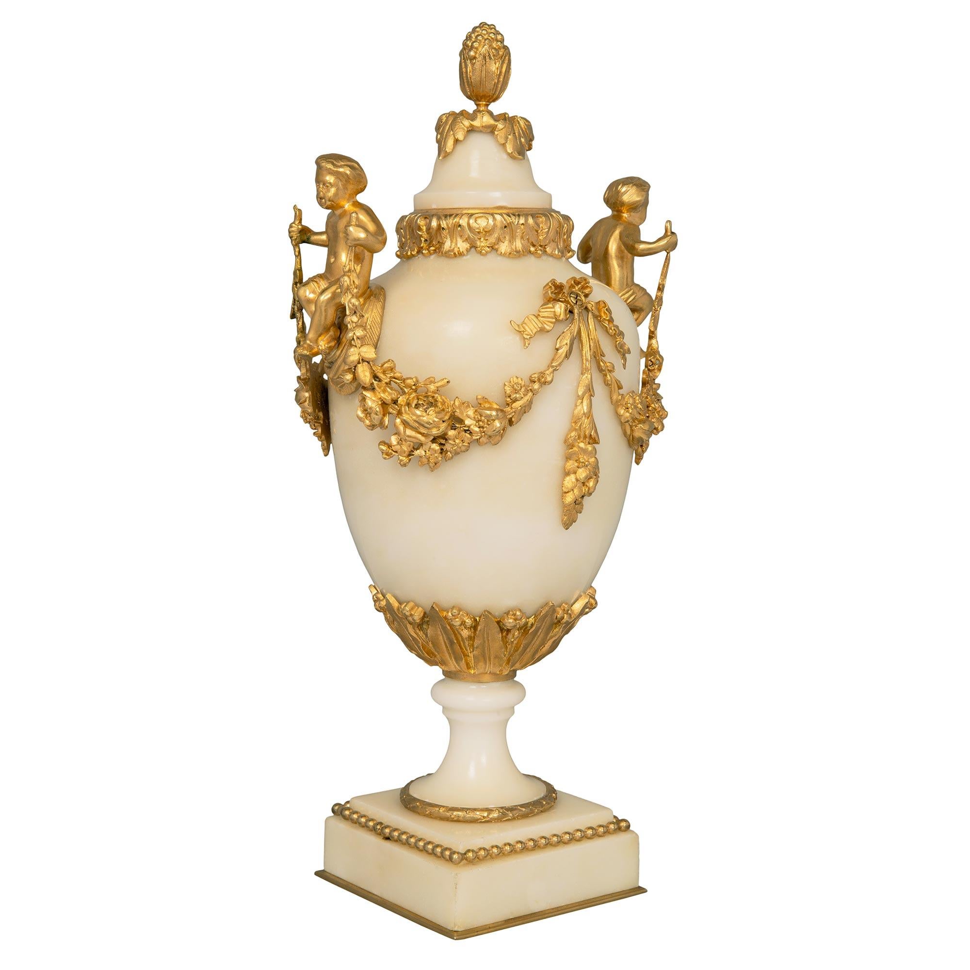 A most elegant pair of French 19th century Louis XVI st. ormolu and white Carrara marble urns. Each urn is raised by a square base with a fine bottom ormolu fillet and a wrap around beaded band. Below the socle pedestals are fine berried laurel