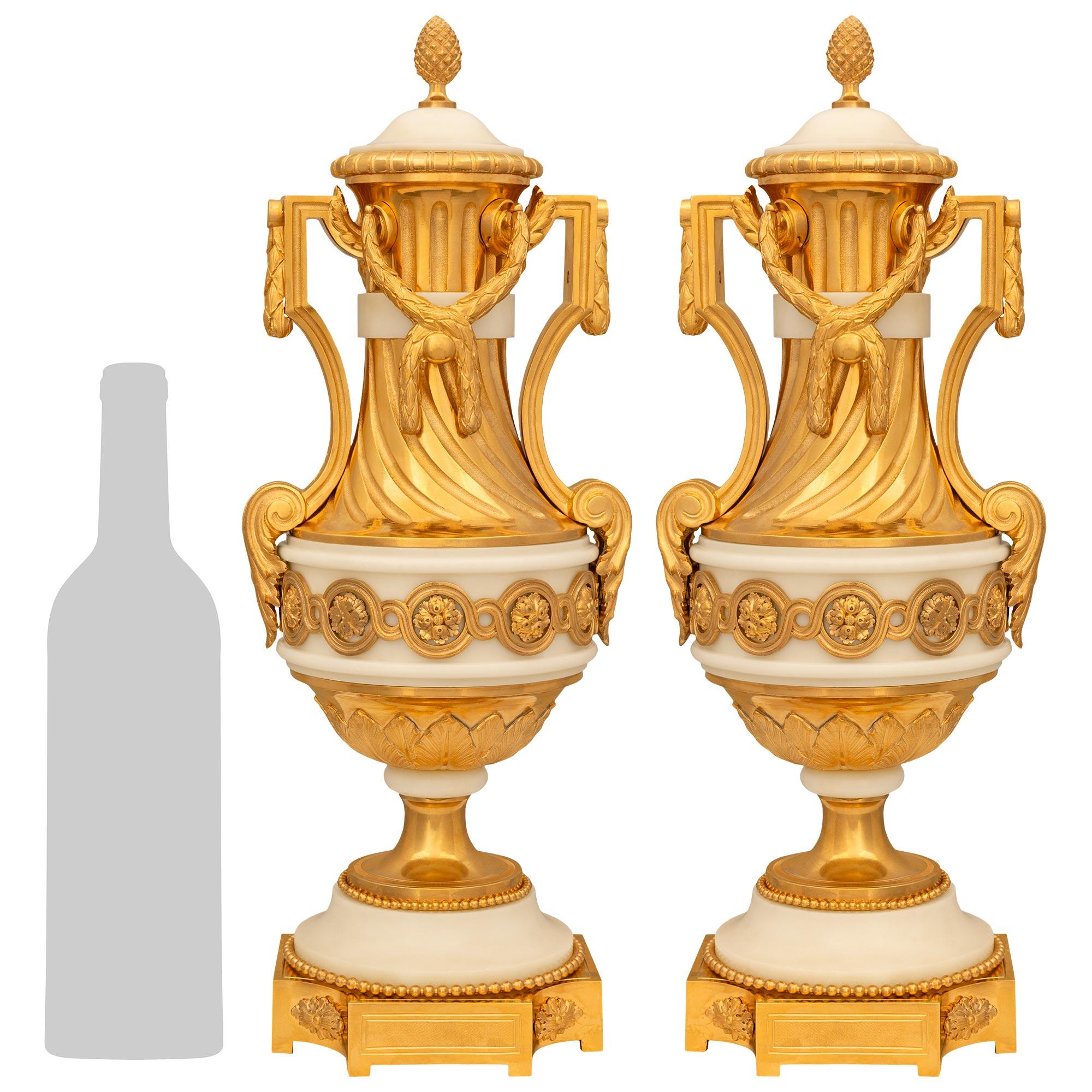 Una splendida coppia di urne francesi del XIX secolo in stile Luigi XVI in ormolu e marmo bianco di Carrara. Ogni elegantissima urna con coperchio poggia su una base quadrata in Ormolu con angoli concavi accentuati da rosette. Sopra c'è un supporto