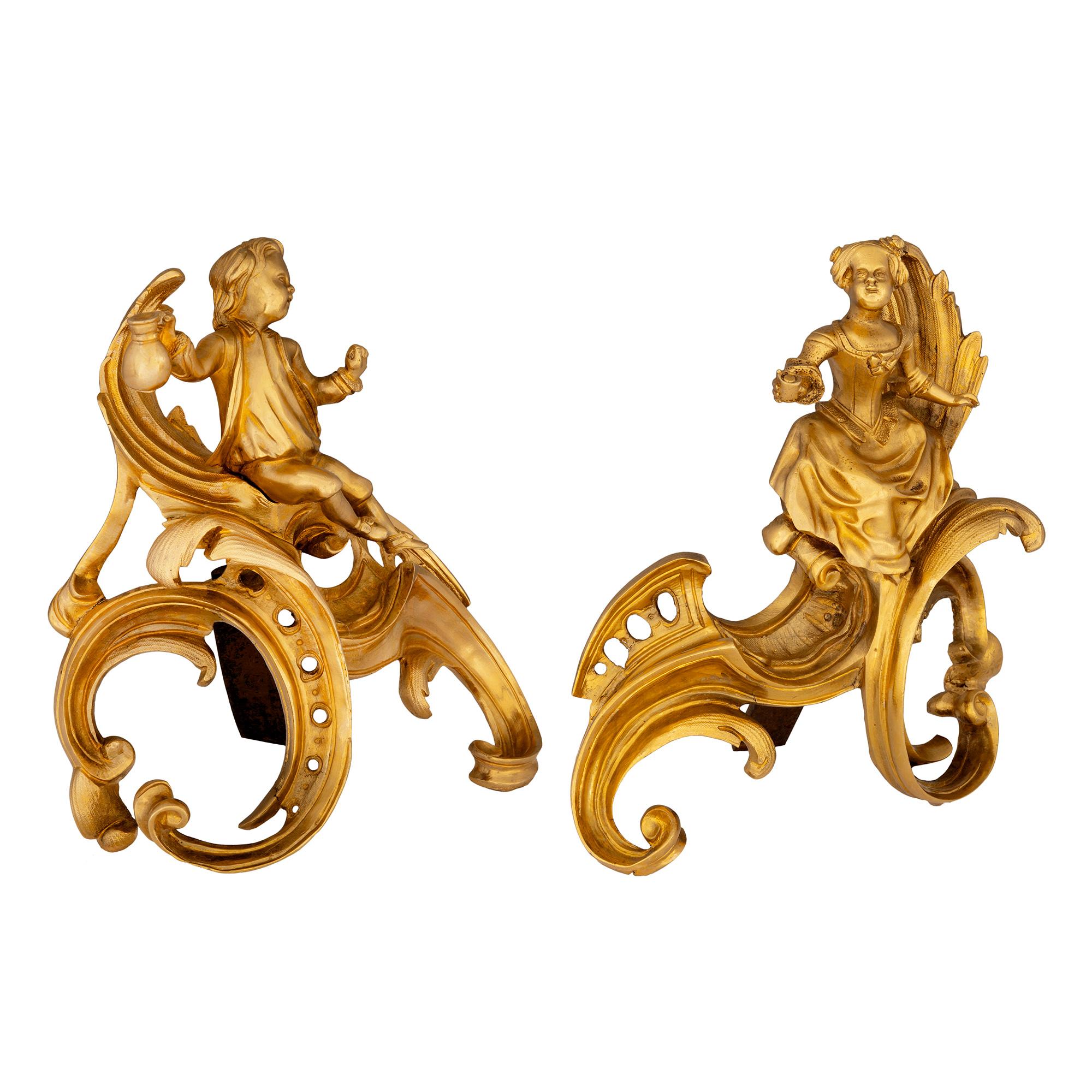 A beautiful and exceptional quality pair of French 19th century Louis XVI st. ormolu andirons. Each fire-gilded andiron is raised by most decorative fanciful scrolled supports with pierced and mottled designs. Above are two charming personages