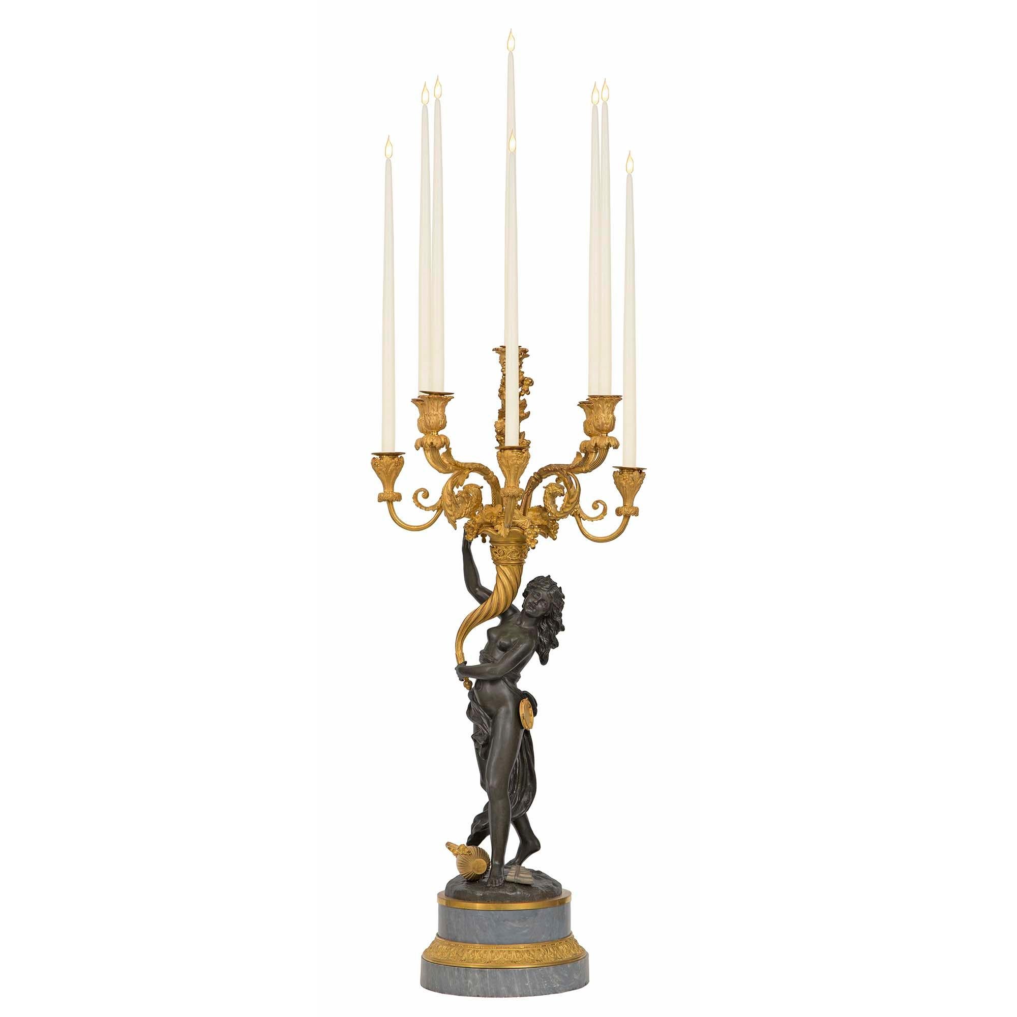 An exquisite and large scale true pair of French 19th century Louis XVI st. ormolu, patinated bronze and marble candelabras, after a model by Clodion. Each candelabra is raised by a striking stepped Bleu Turquin marble base, with a fine wrap around