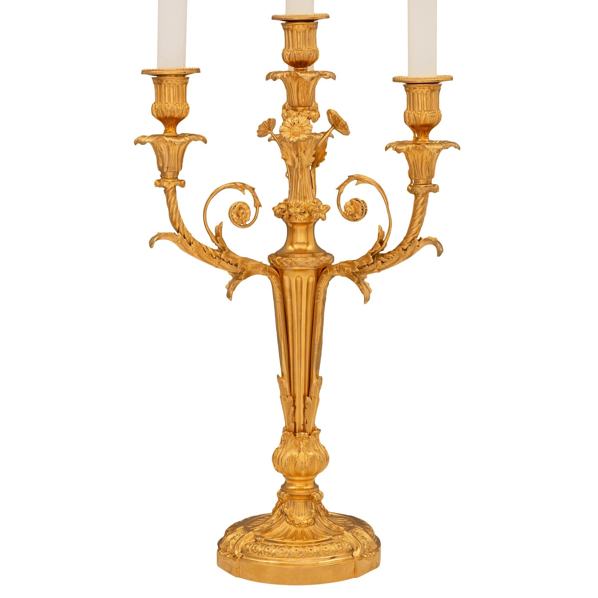 An elegant pair of French 19th century Louis XVI st. ormolu candelabra lamps. Each four arm lamp is raised by a circular base with a finely mottled wrap around band, striking interlocking geometric designs, lovely scrolled foliate movements, swaging