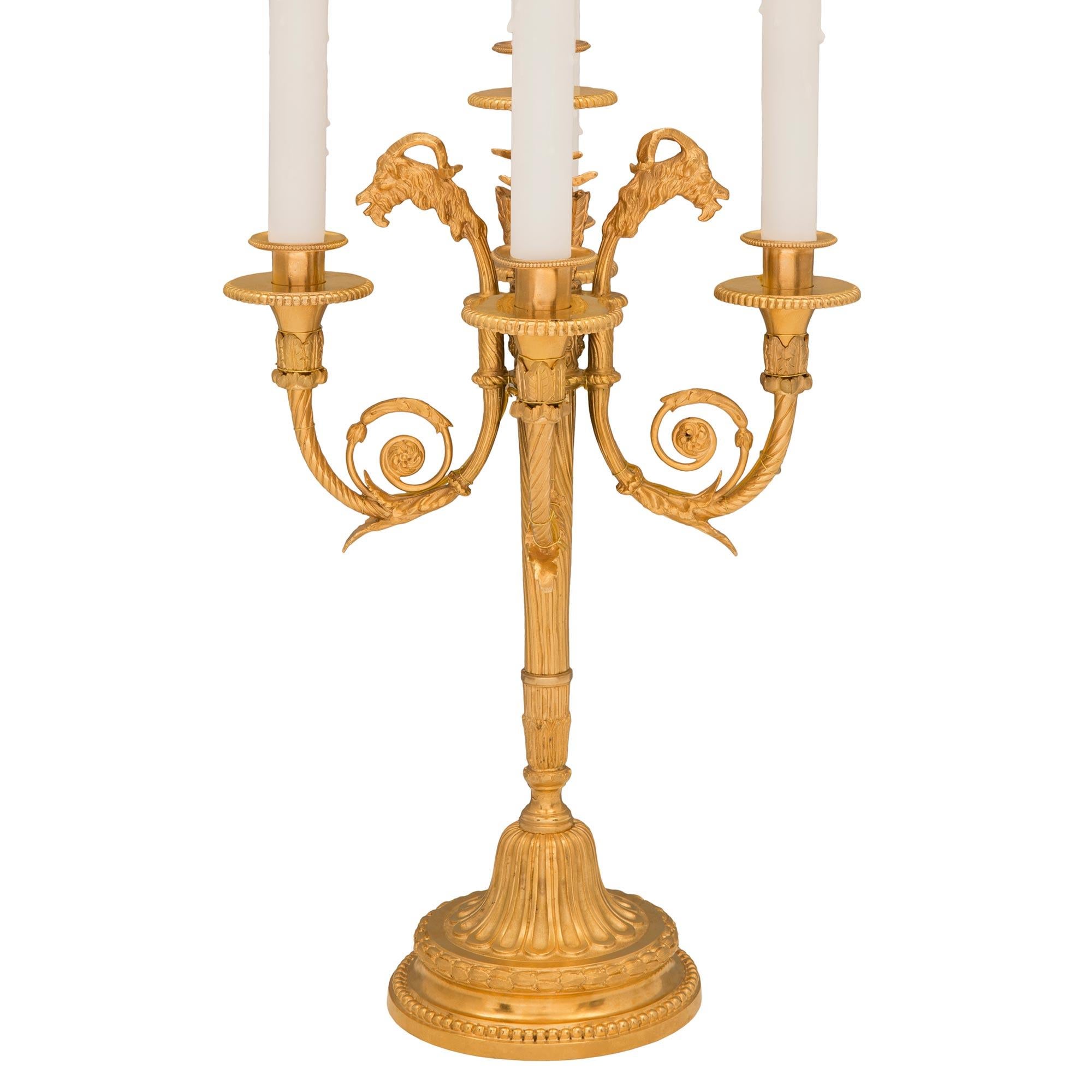 Un'elegantissima coppia di lampade a candelabro francesi del XIX secolo in stile Luigi XVI. Ciascuna lampada a cinque bracci è sollevata da una base circolare screziata con una fascia di perline e alloro boscoso riccamente cesellato. Il piedistallo