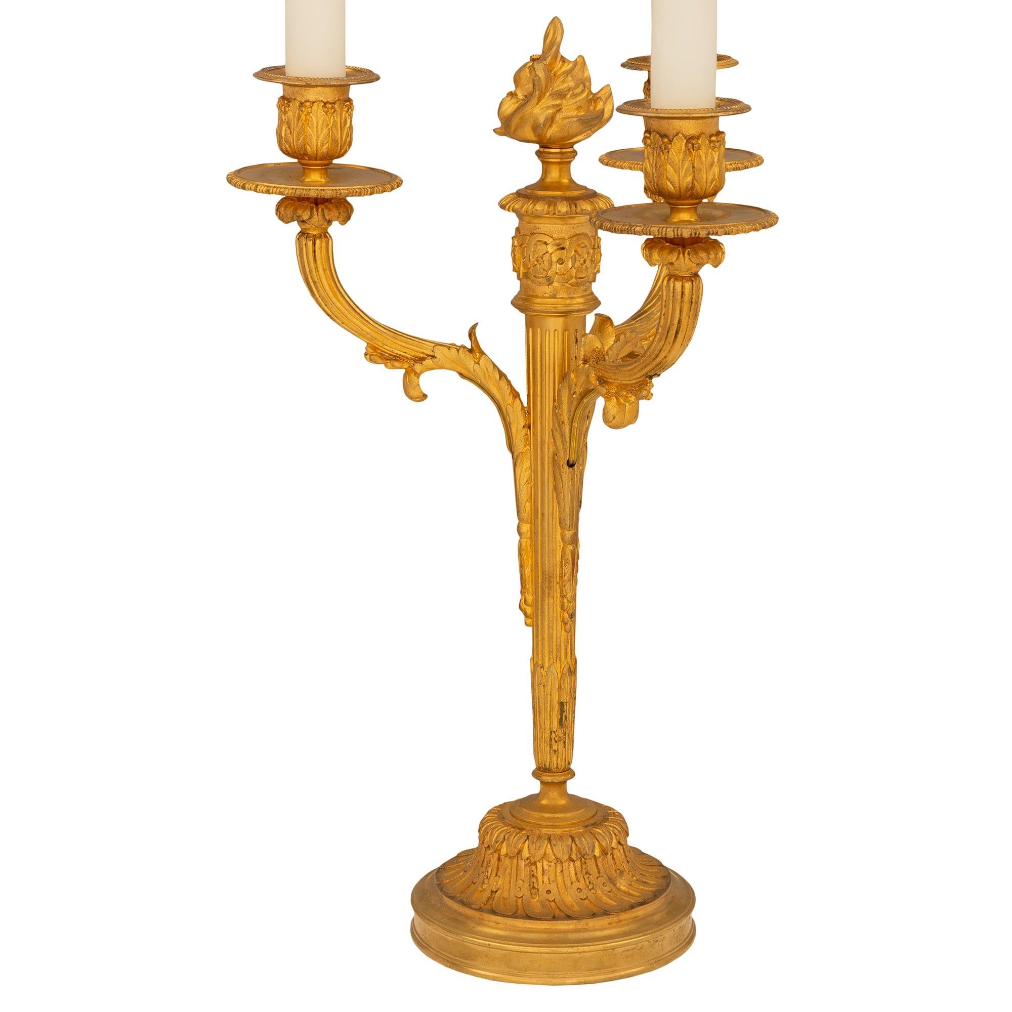 Une très belle paire de lampes candélabres en bronze doré de style Louis XVI du 19ème siècle. Chaque lampe à trois bras est surélevée par une base circulaire avec une fine bordure mouchetée et de magnifiques motifs feuillus cannelés en spirale