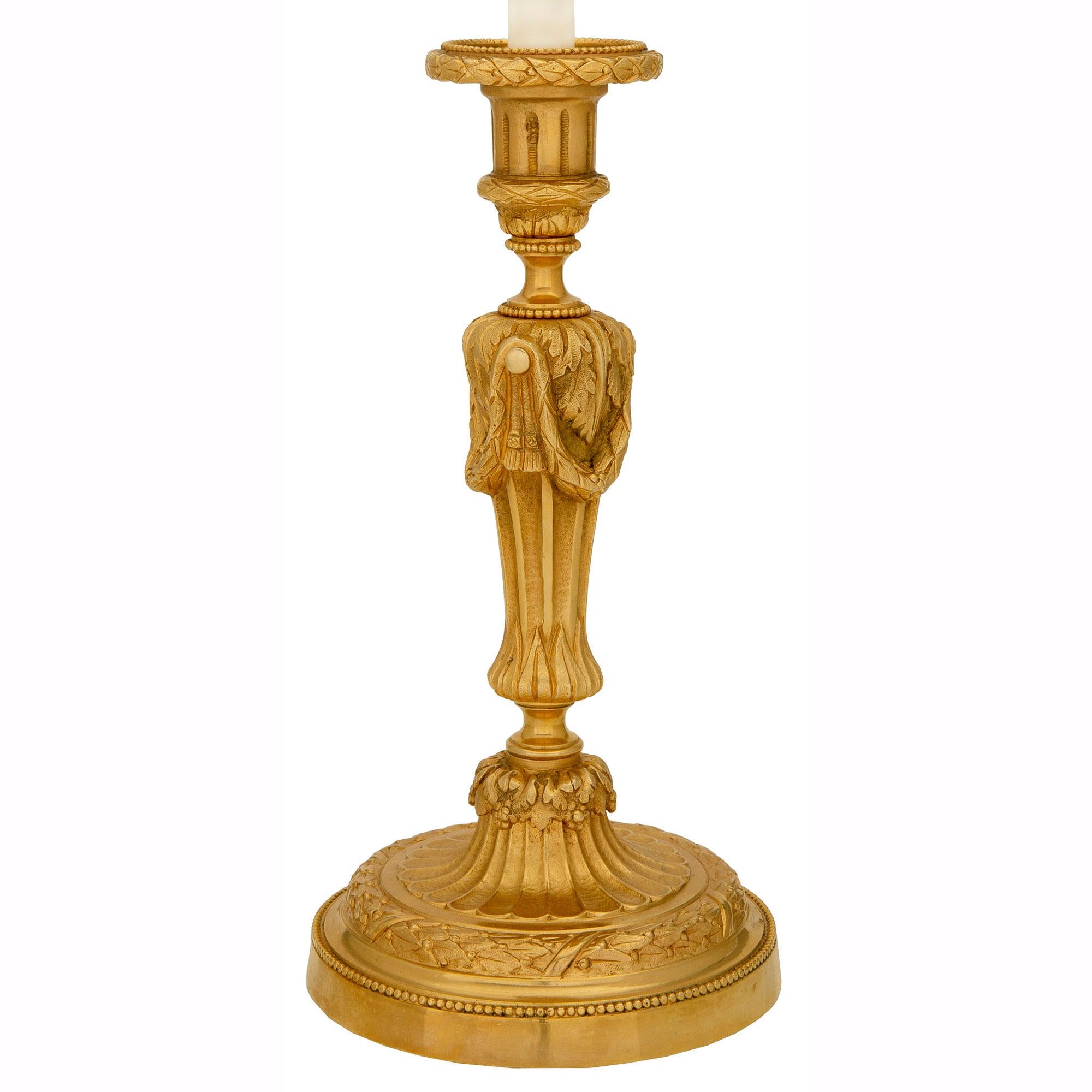 Une paire élégante et de haute qualité de chandeliers en bronze doré de style Louis XVI et d'époque Belle Époque. Chaque chandelier est surélevé par une base circulaire avec une fine bande perlée et une couronne de laurier liée richement ciselée.