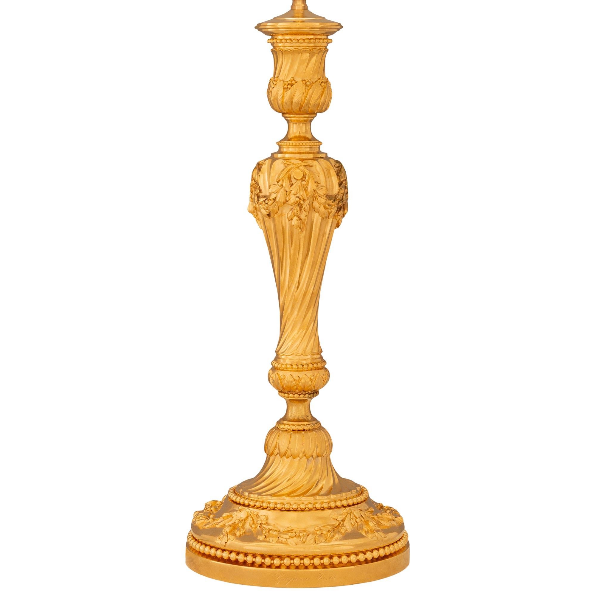 Une paire de lampes en bronze doré de style Louis XVI du XIXe siècle, signée Gagneau Paris. Chaque lampe est surmontée d'un piédestal circulaire avec un bord perlé. Au-dessus du piédestal se trouve le socle décoré de guirlandes de feuillage, d'un