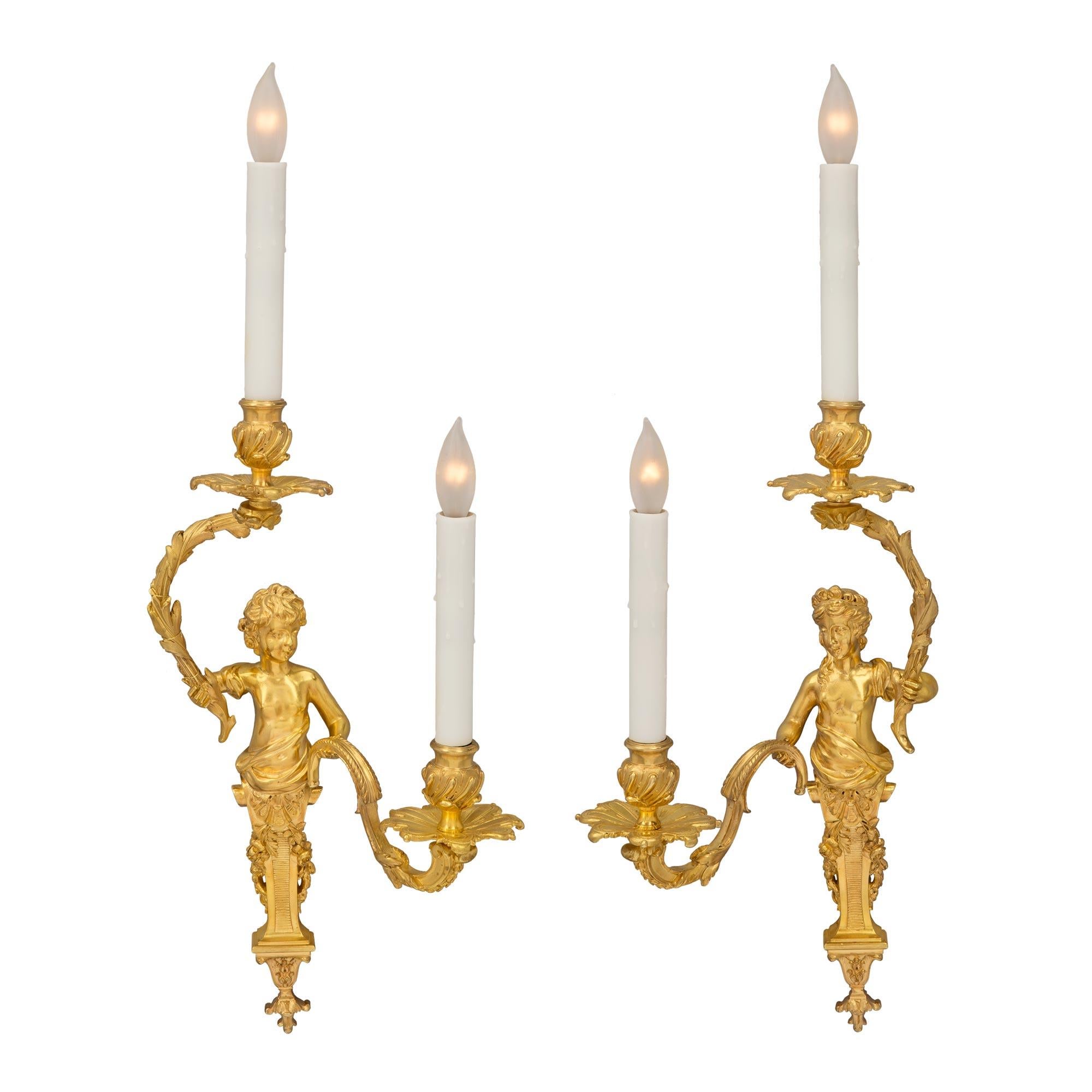 A striking and high quality true pair of French 19th century Louis XVI st. ormolu two arm sconces after a model by Gilles-Marie Oppenordt and attributed to Henry Dasson. Each sconce is centered by a lovely foliate bottom finial below the elegant