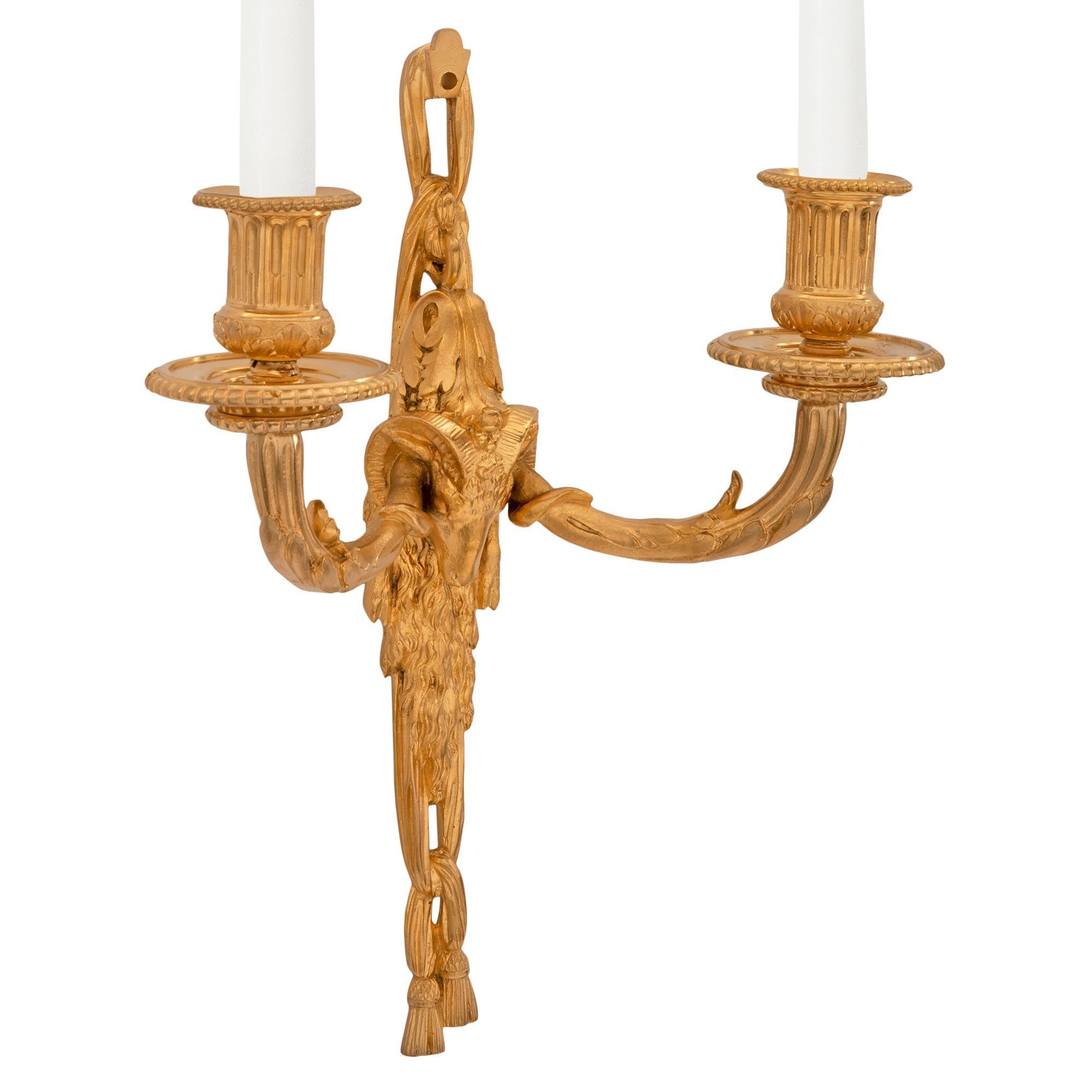 An elegant and very high quality pair of French 19th century Louis XVI st. ormolu sconces. Each two arm sconce is centered by charming and wonderfully executed tied garland tassels below the richly chased rams head amidst fur and striking acanthus