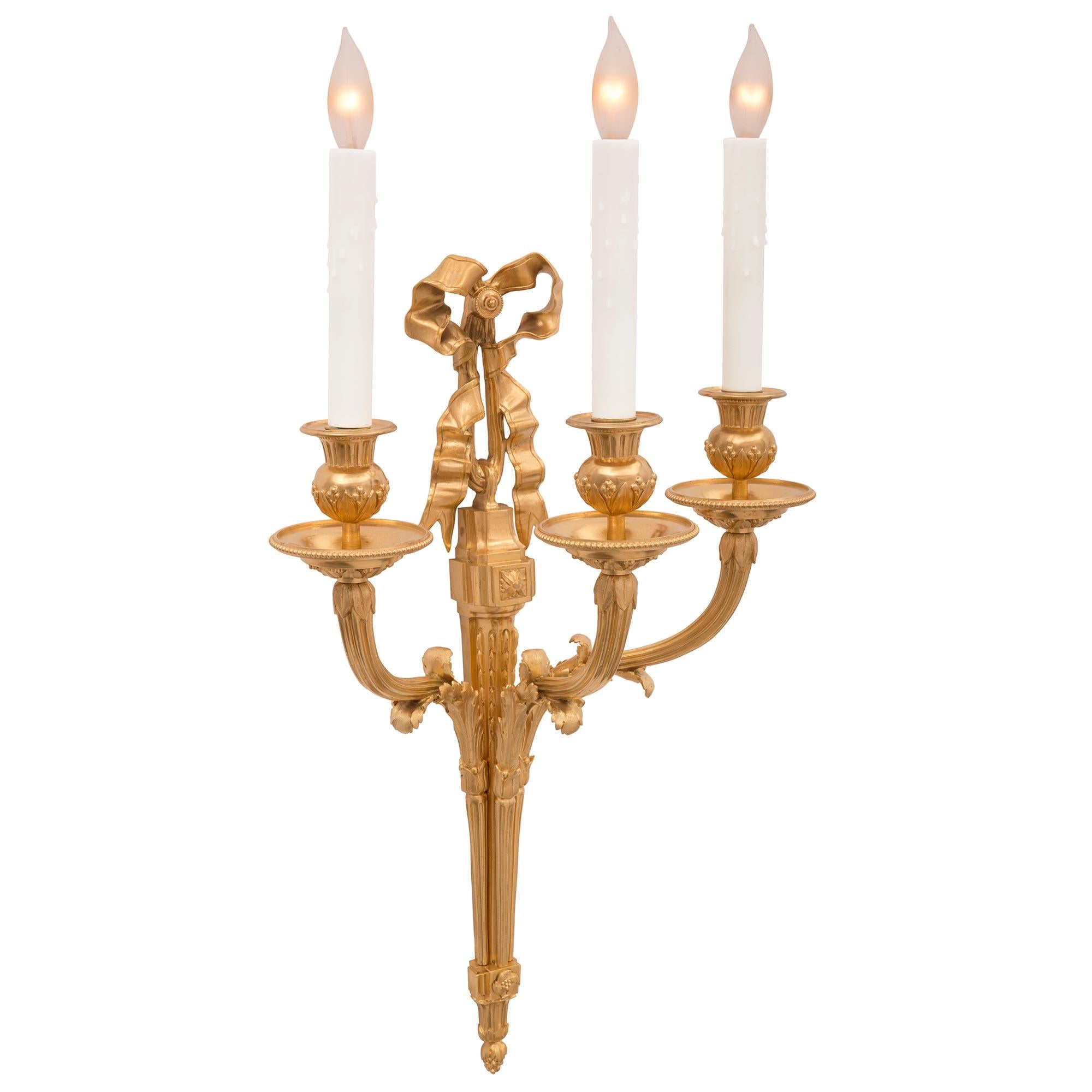 Ein elegantes Paar französischer Ormolu-Leuchter aus dem 19. Jahrhundert im Stil Louis XVI. Jede dreiarmige Leuchte wird von einer fein detaillierten Eichelspitze unter dem eleganten, konisch zulaufenden Korpus gekrönt. Die Oberseite der