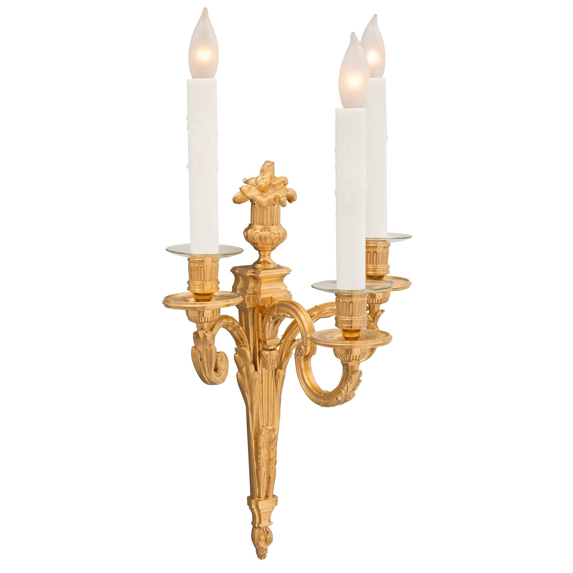 An extremely elegant and high quality pair of French 19th century Louis XVI st. ormolu sconces. Each three arm sconce is centered by a richly chased bottom floral finial in a striking satin and burnished finish below the tapered central fut