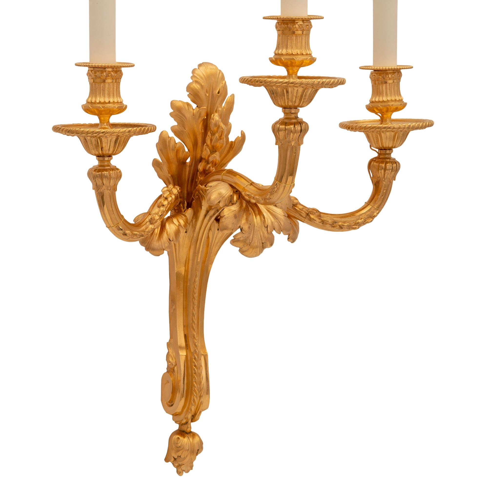 Elegantísimo par de apliques franceses de ormolina del siglo XIX, estilo Luis XVI. Cada candelabro de tres brazos está centrado por un precioso remate inferior foliado debajo del hermoso soporte central con volutas y una gran hoja de acanto