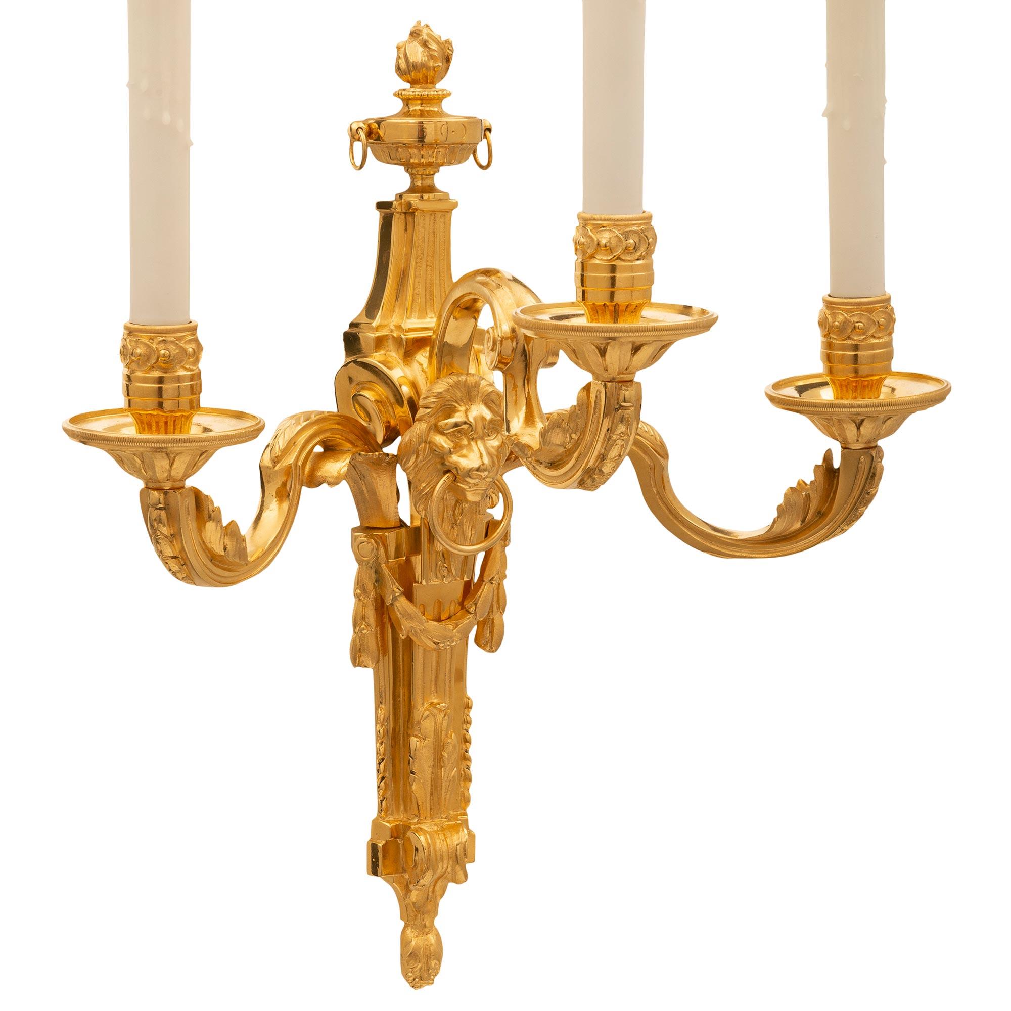 A striking and most elegant pair of French 19th century Louis XVI st. ormolu sconces. Each three arm sconce is centered by beautiful backplates with richly chased foliate designs, lovely swaging berried laurel garlands, handsome lion heads with