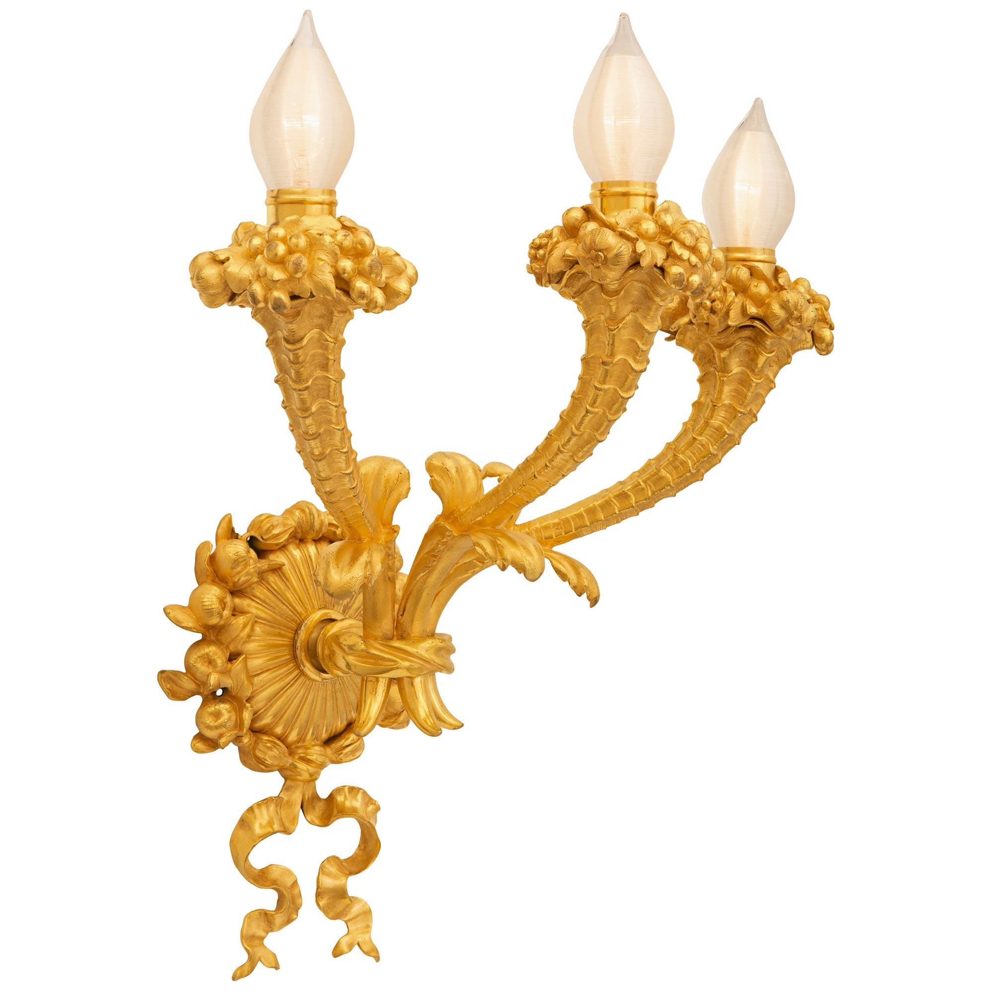 Une paire sensationnelle et extrêmement décorative d'appliques en bronze doré de style Louis XVI du 19ème siècle. Chaque applique à trois bras est centrée par une plaque arrière anglée frappante avec de charmantes guirlandes florales finement
