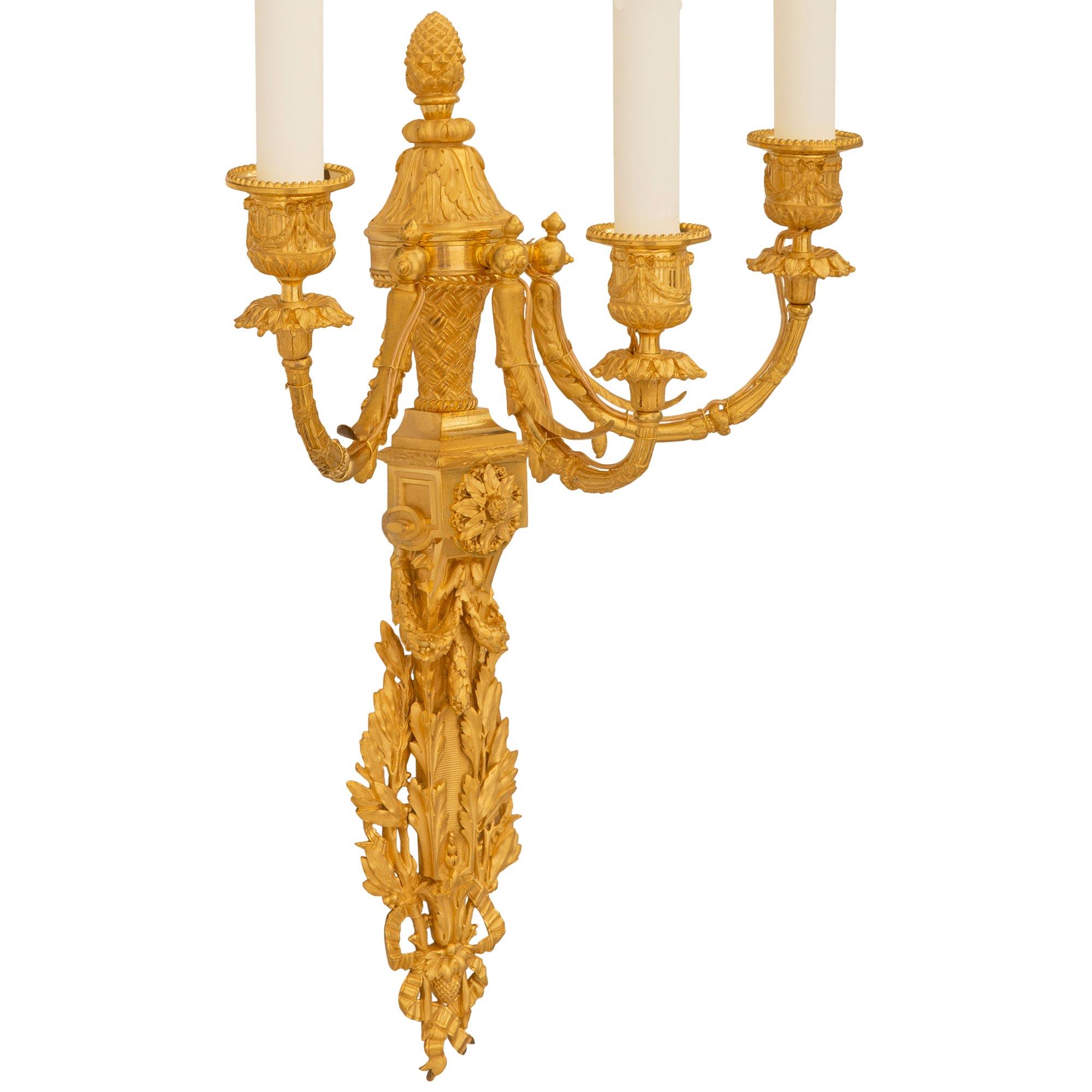 A striking and high quality pair of French 19th century Louis XVI st. Ormolu sconces. Each three arm sconce is centered by a lower backplate with a reeded design flanked by large scale laurel branches tied with a ribbon. Above is a stunning reserve