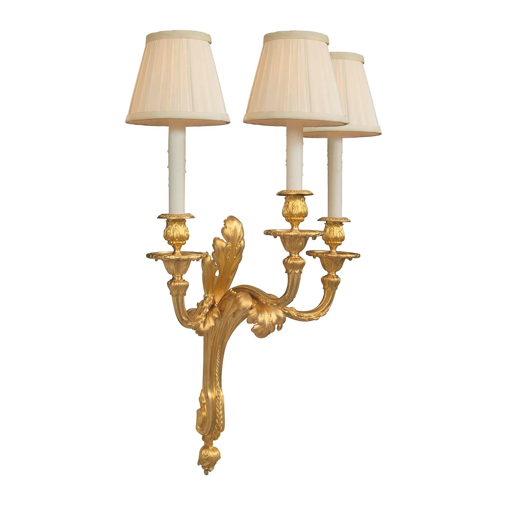 An extremely elegant and high quality pair of French 19th century Louis XVI st. ormolu three arm sconces. Each sconce is centered by a fine foliate bottom finial below the beautiful scrolled central support. The three finely scrolled arms display