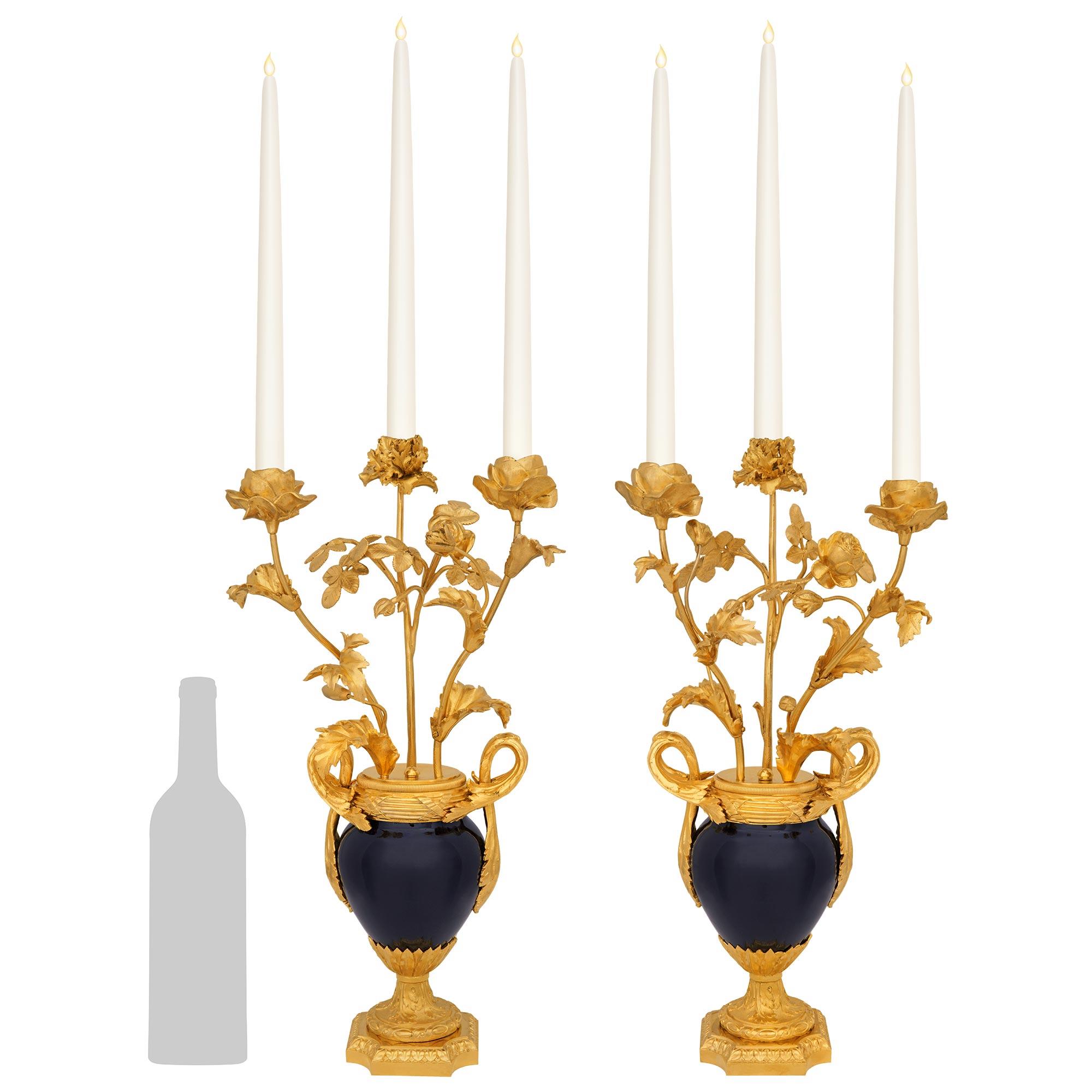 Impresionante pareja de candelabros franceses de tres brazos de porcelana de Sèvres azul cobalto y ormolu del siglo XIX, estilo Luis XVI. Cada candelabro se eleva sobre una base cuadrada moteada de ormolu con esquinas cóncavas y una fina banda de