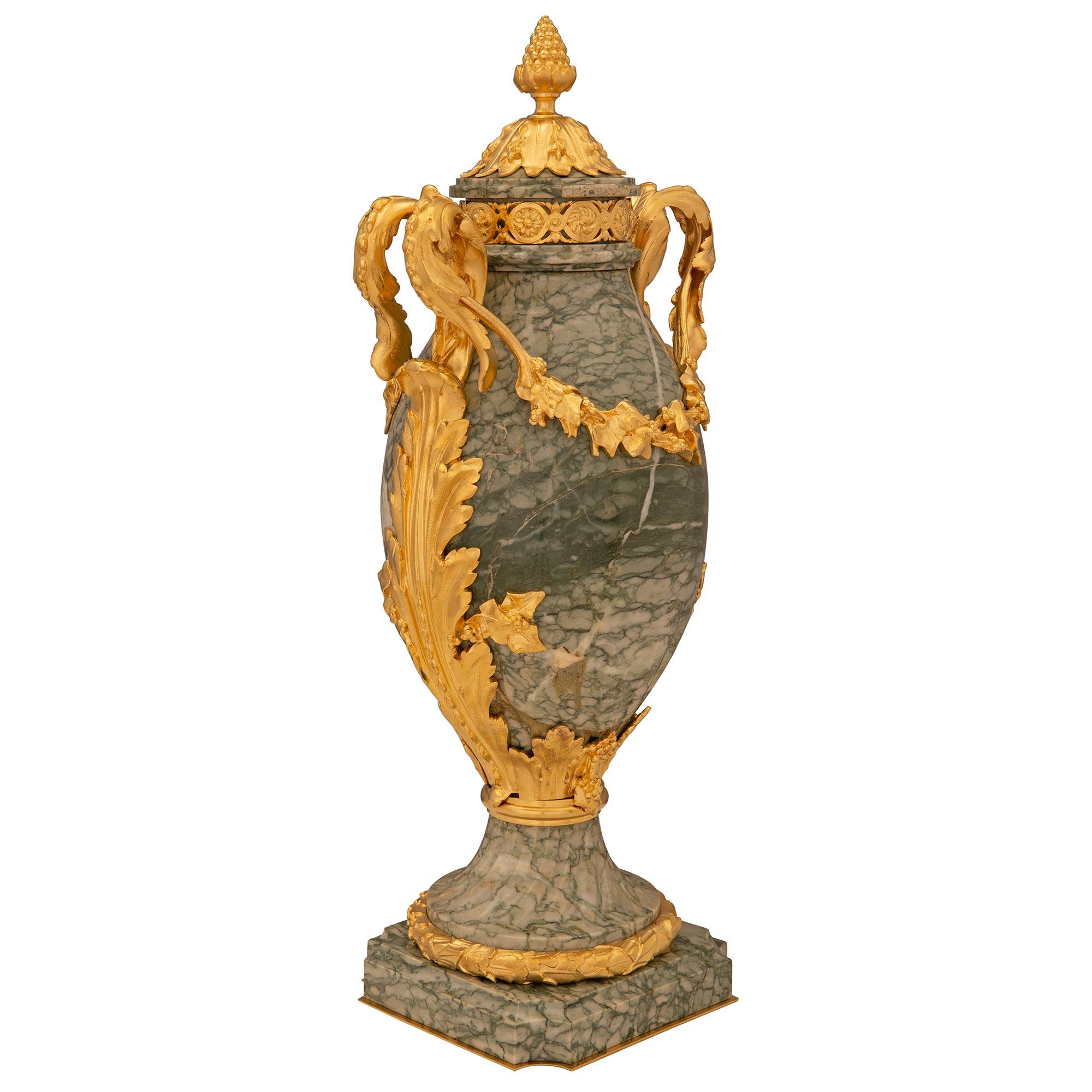 A stunning true pair of French 19th century Louis XVI st. Vert Campan marble and ormolu urns. Each urn is raised by an elegant square base with concave corners, a fine mottled border, and a delicate bottom ormolu fillet. The socle shaped pedestal