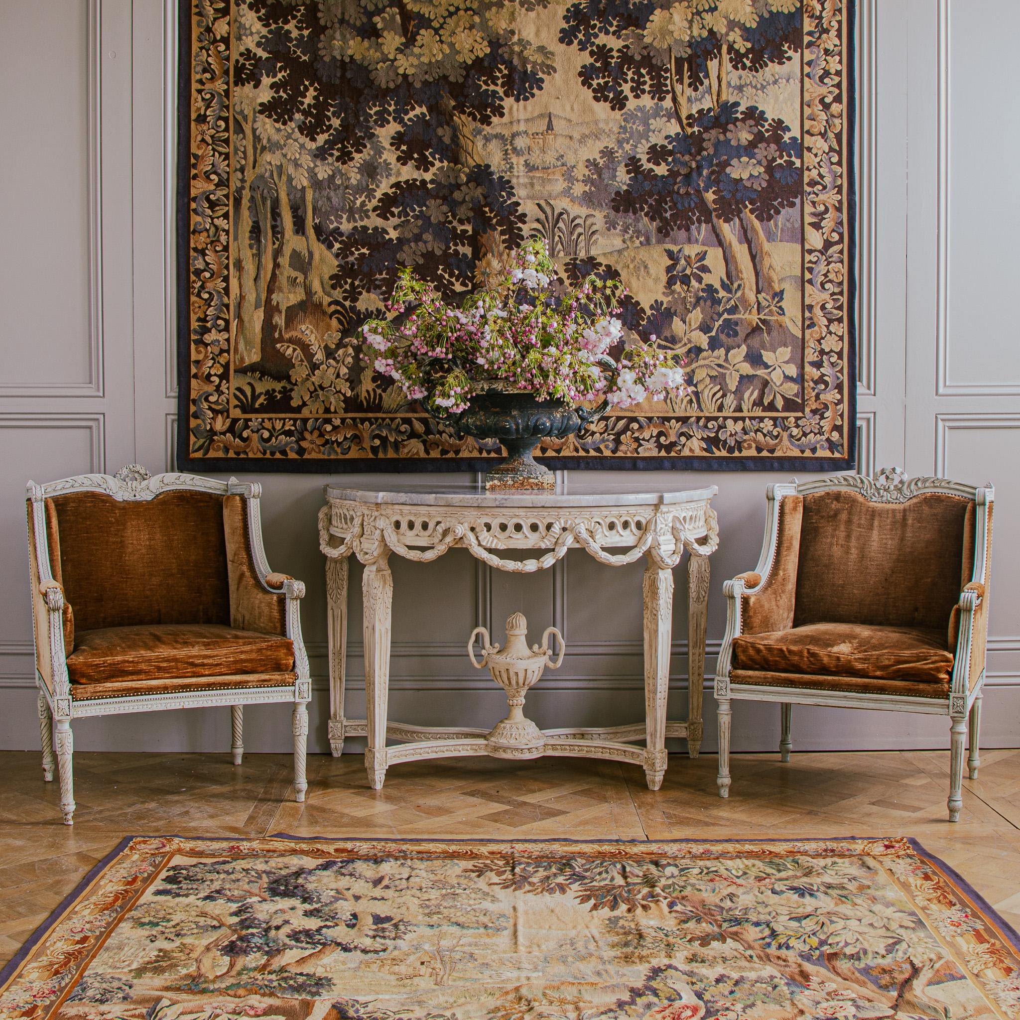 A pair of French Louis XVI style armchairs, 'bergères à oreilles', circa 1880. Created in France, during the 19th century. These chairs feature a wingback design with hand carved motifs of ribbons, flanked with petite flowers and foliage adorning