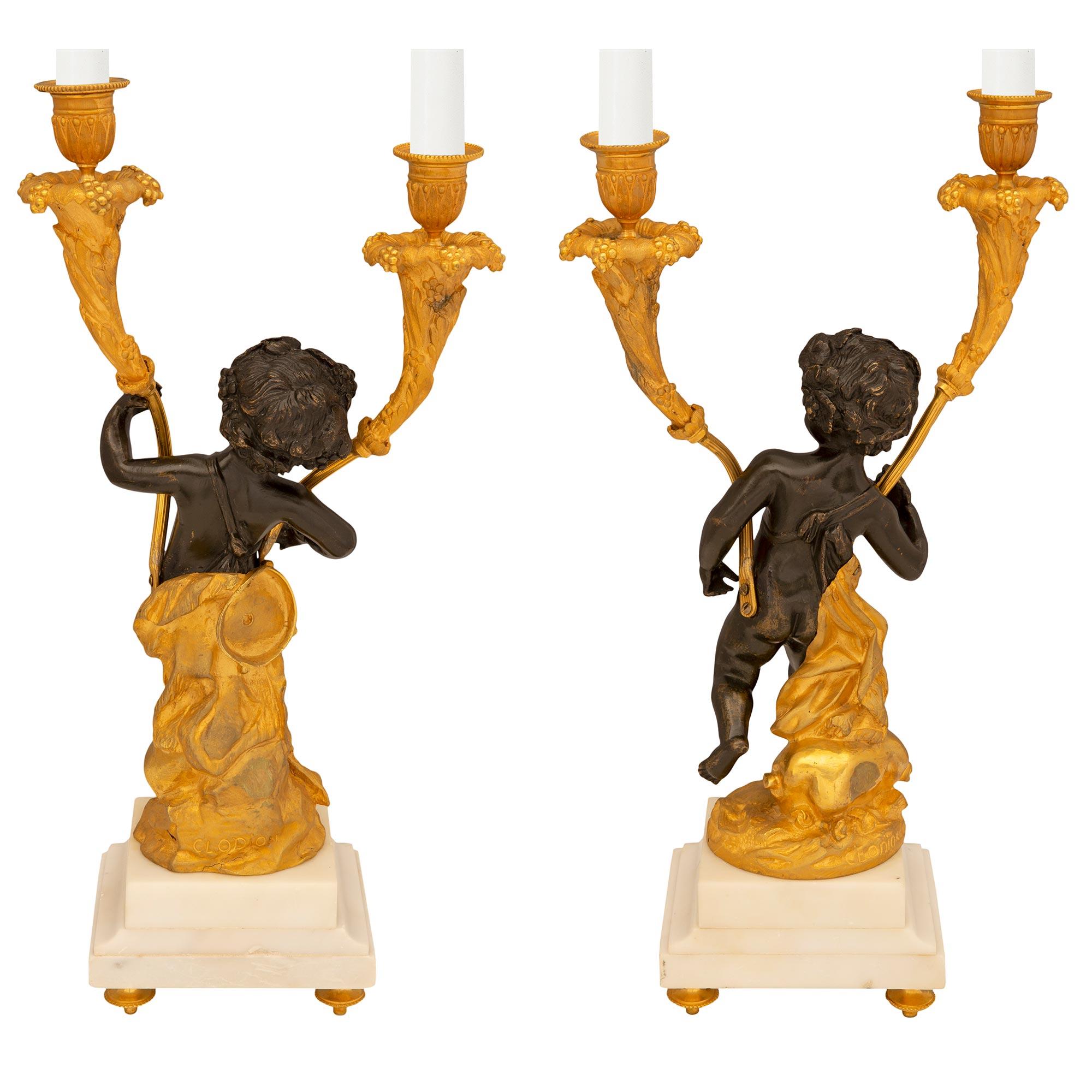 An elegant true pair of French 19th century Louis XVI st. ormolu, patinated bronze and white Carrara marble candelabras, signed Clodion. Each two arm candelabra is raised by fine topie shaped ormolu feet below a square white Carrara marble base. The