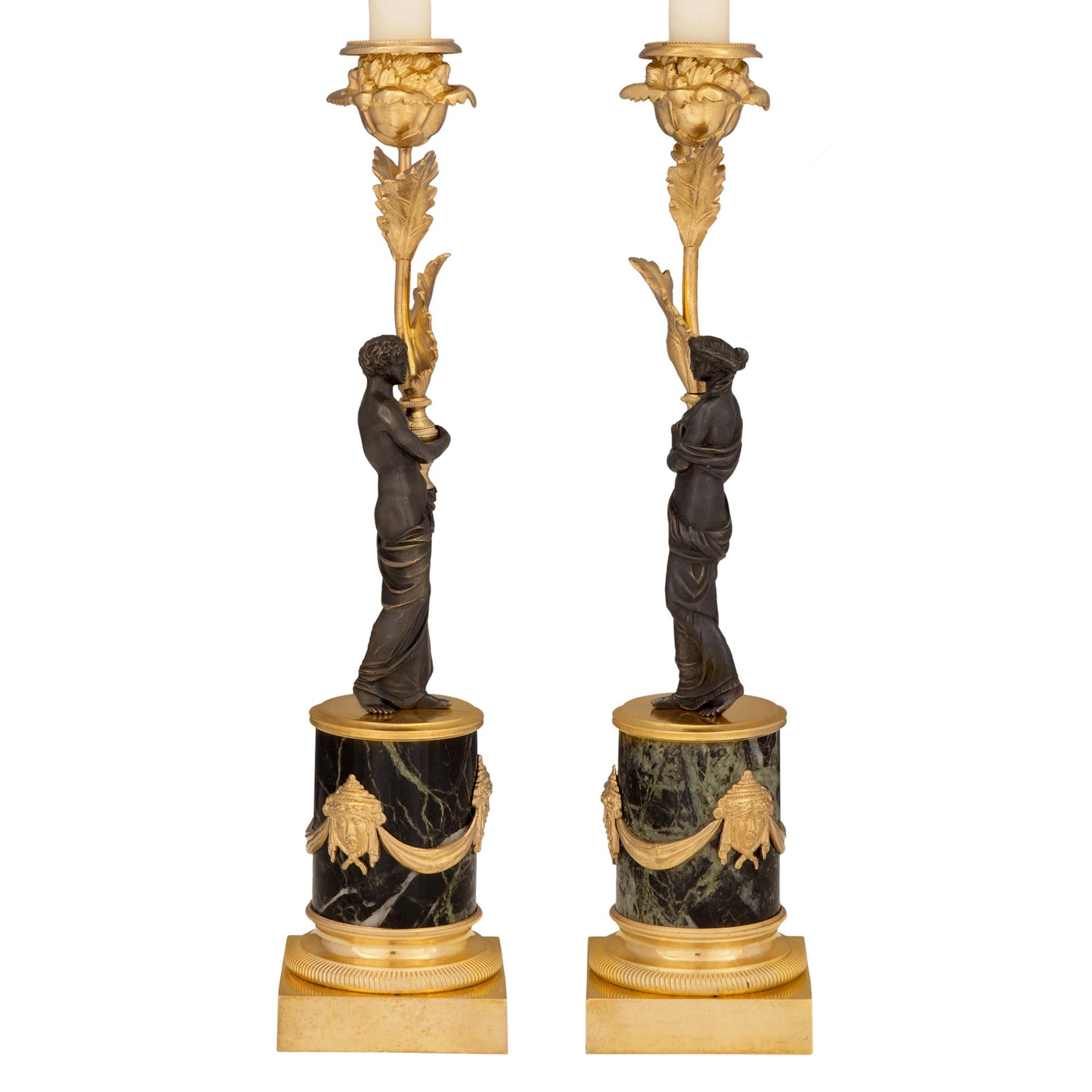 Un'impressionante coppia di candelieri francesi del XIX secolo in stile Luigi XVI, ormolu, bronzo patinato e marmo Vert de Patricia. Ciascun candeliere è sollevato da una base quadrata in ormù, da un piedistallo a socle e da una sottile fascia