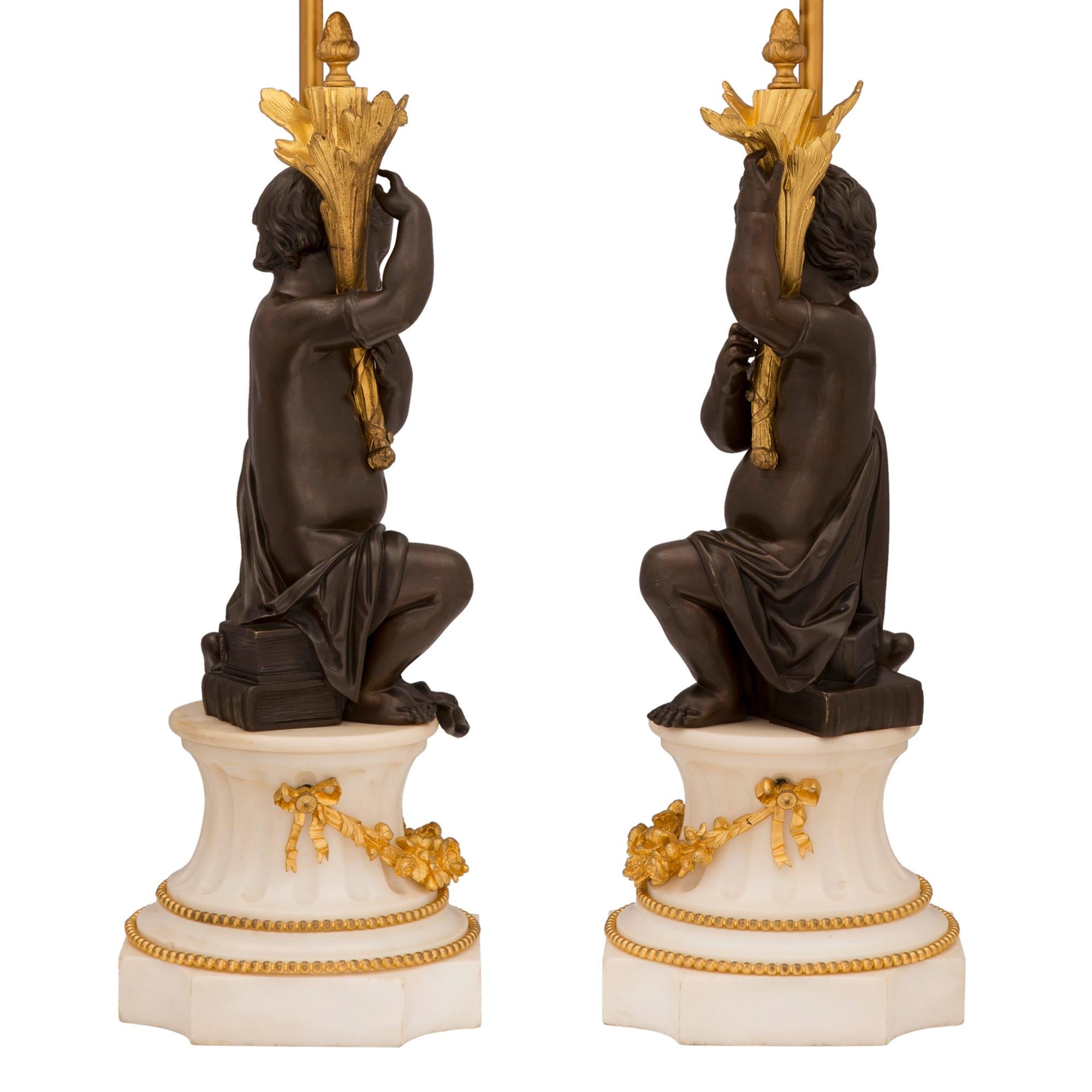 Une paire très élégante de lampes françaises du 19ème siècle, de style Louis XVI, en bronze patiné, bronze doré et marbre blanc de Carrare. Chaque lampe est surélevée par une base carrée en marbre de Carrare blanc aux angles concaves et un
