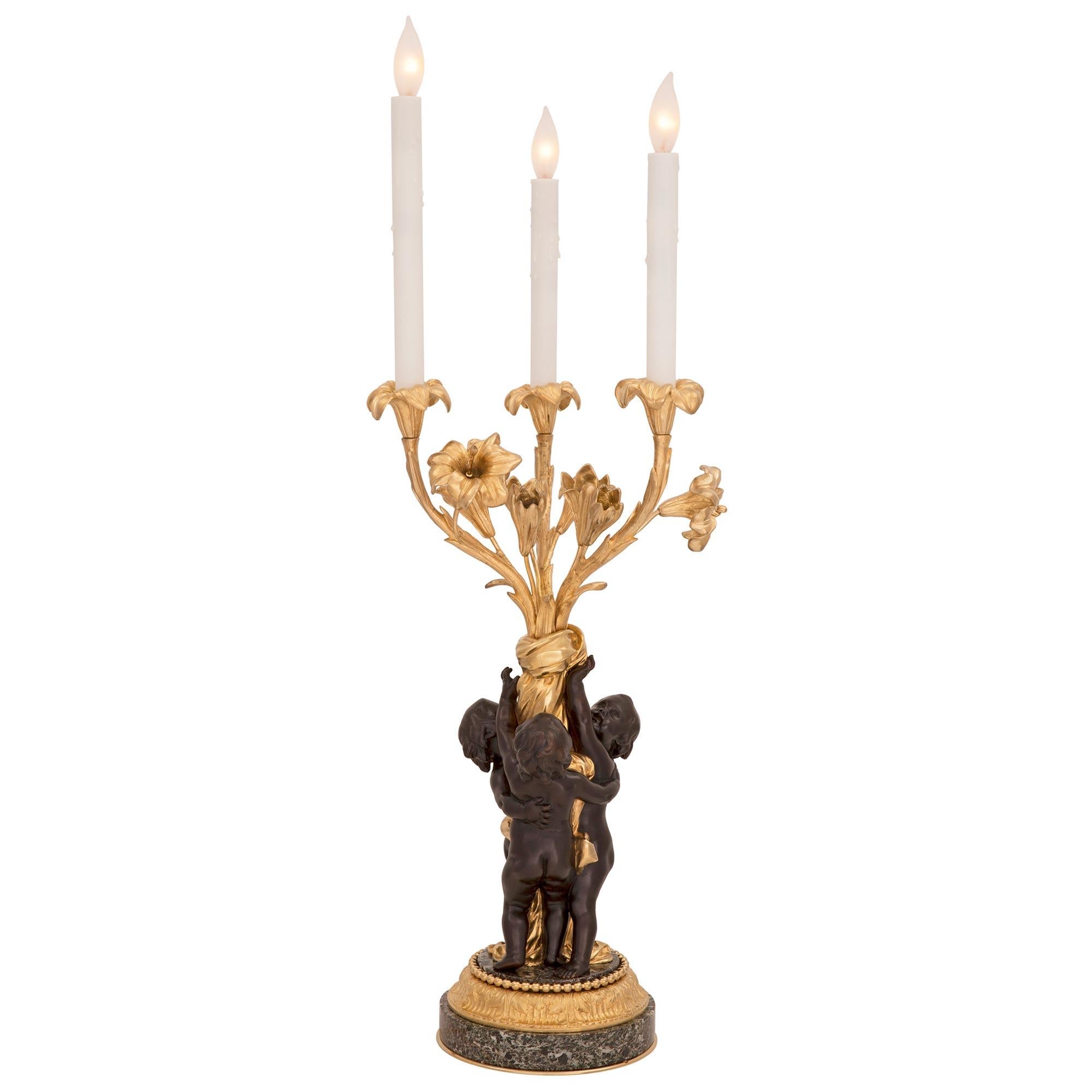 An exquisite pair of French 19th century Louis XVI st. patinated bronze, ormolu and Vert de Patricia marble candelabra lamps. Each lamp is raised by an elegant circular base with fine bottom ormolu bands and top foliate and beaded wrap around bands.