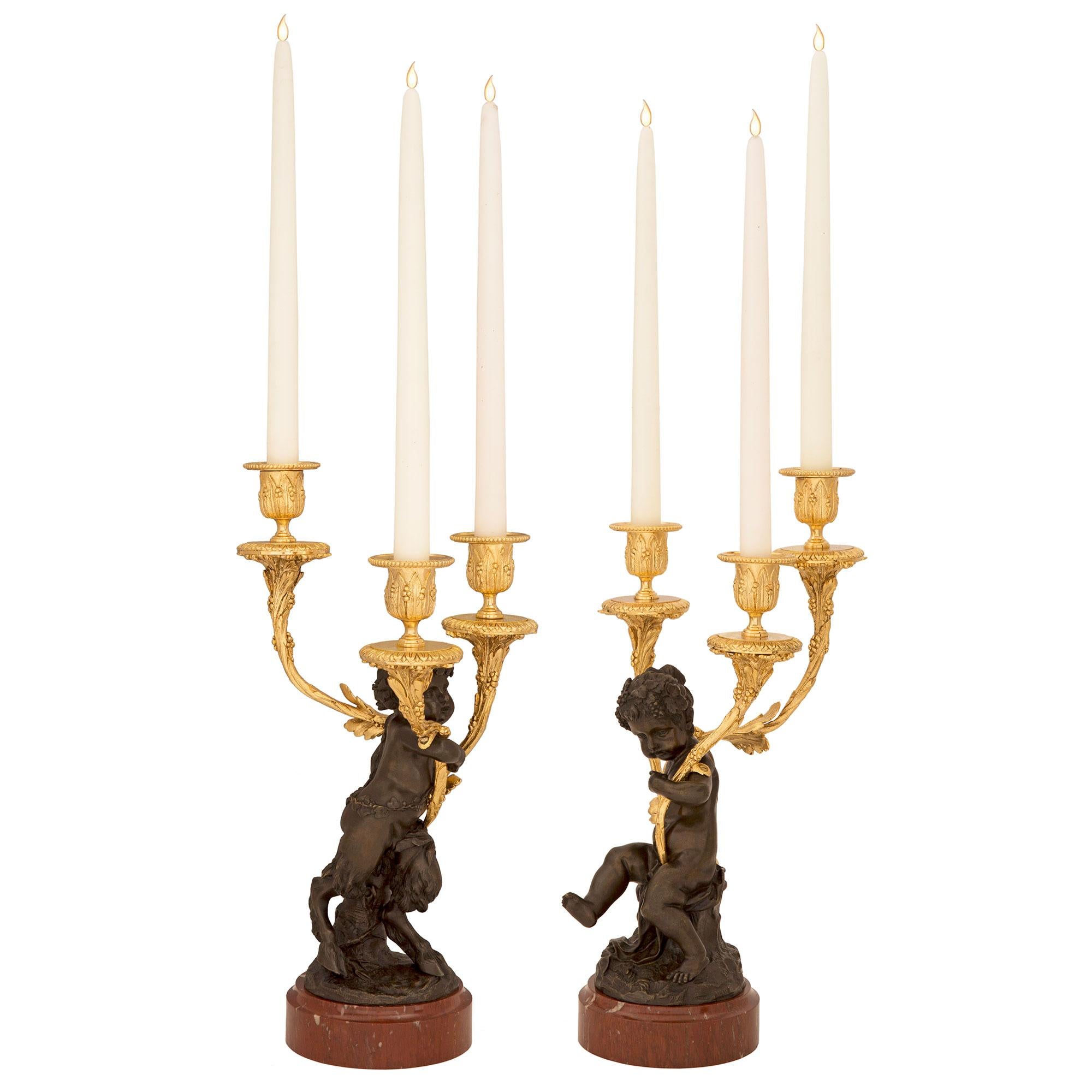 A beautiful and high quality true pair of French 19th century Louis XVI st. ormolu, patinated bronze and Rouge Griotte marble candelabras, attributed to Clodion. Each candelabra is raised by an elegant circular Rouge Griotte marble base with a fine