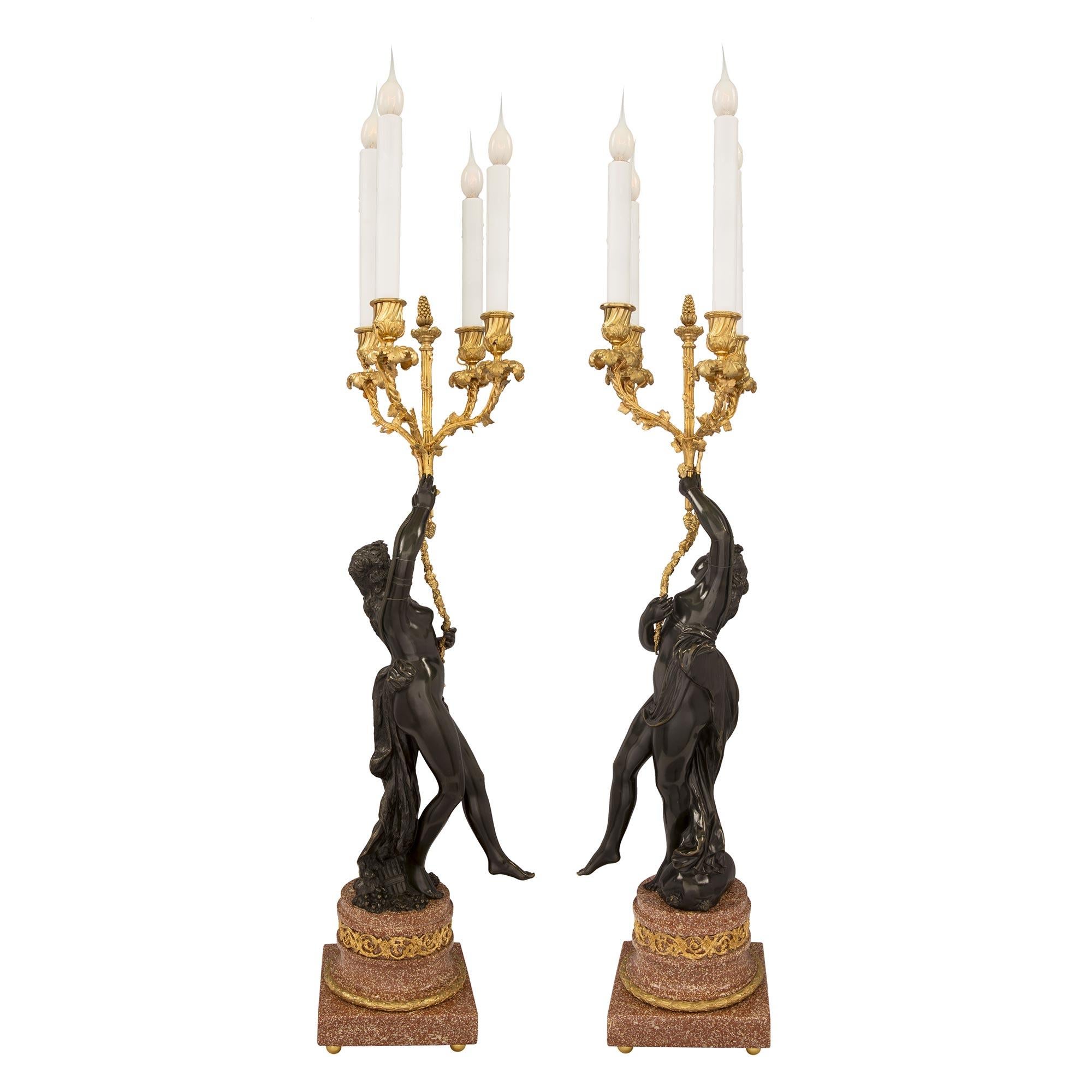 A stunning and high quality true pair of French 19th century Louis XVI st. patinated bronze, ormolu and Porphyry electrified candelabra lamps. Each candelabra is raised by elegant ormolu ball feet below the Porphyry base. The bases display square