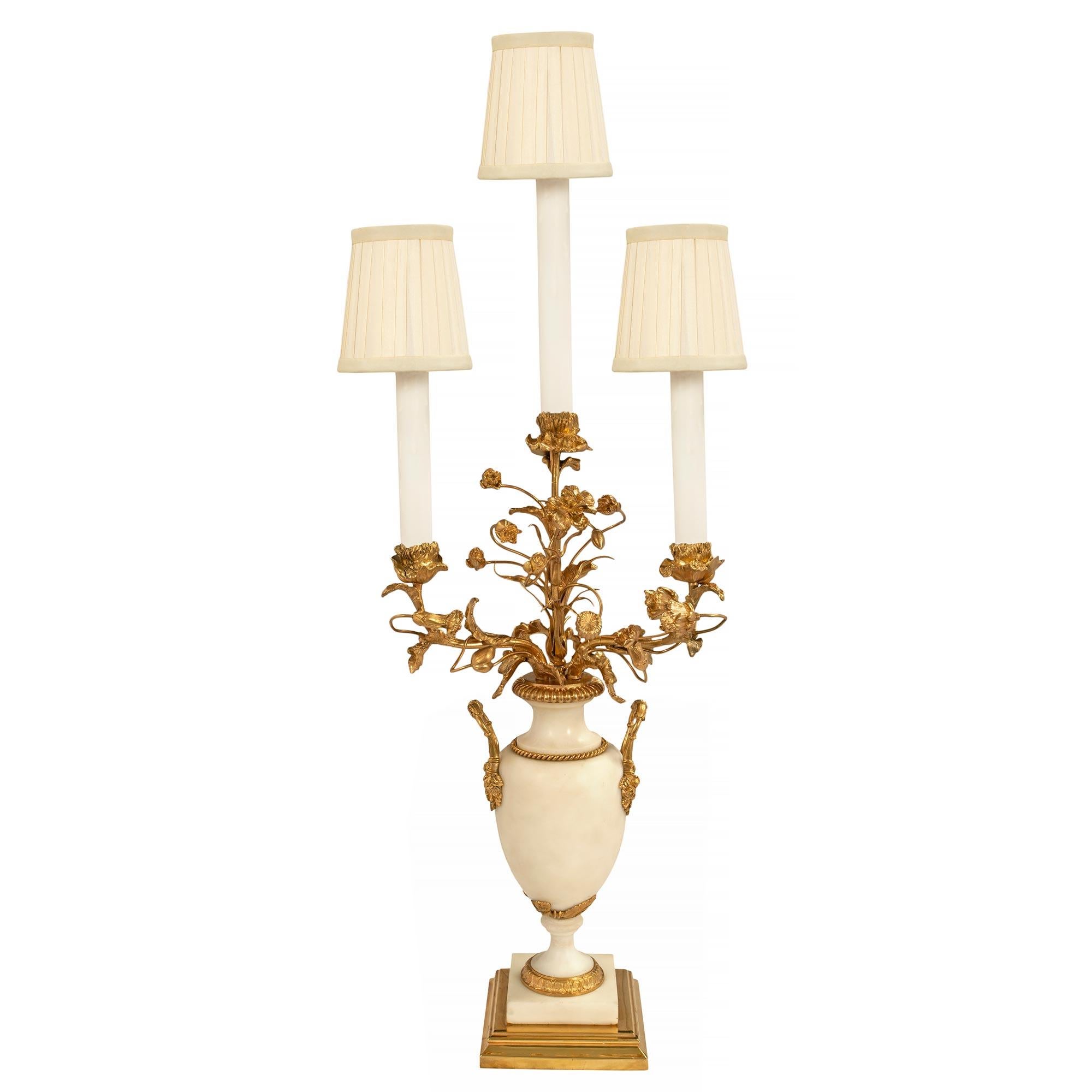 A most attractive pair of French mid 19th century Louis XVI st. white Carrara marble and ormolu mounted electrified candelabras. The pair are raised by square mottled ormolu and marble bases. Above, the socles are elegantly decorated by a coeur de