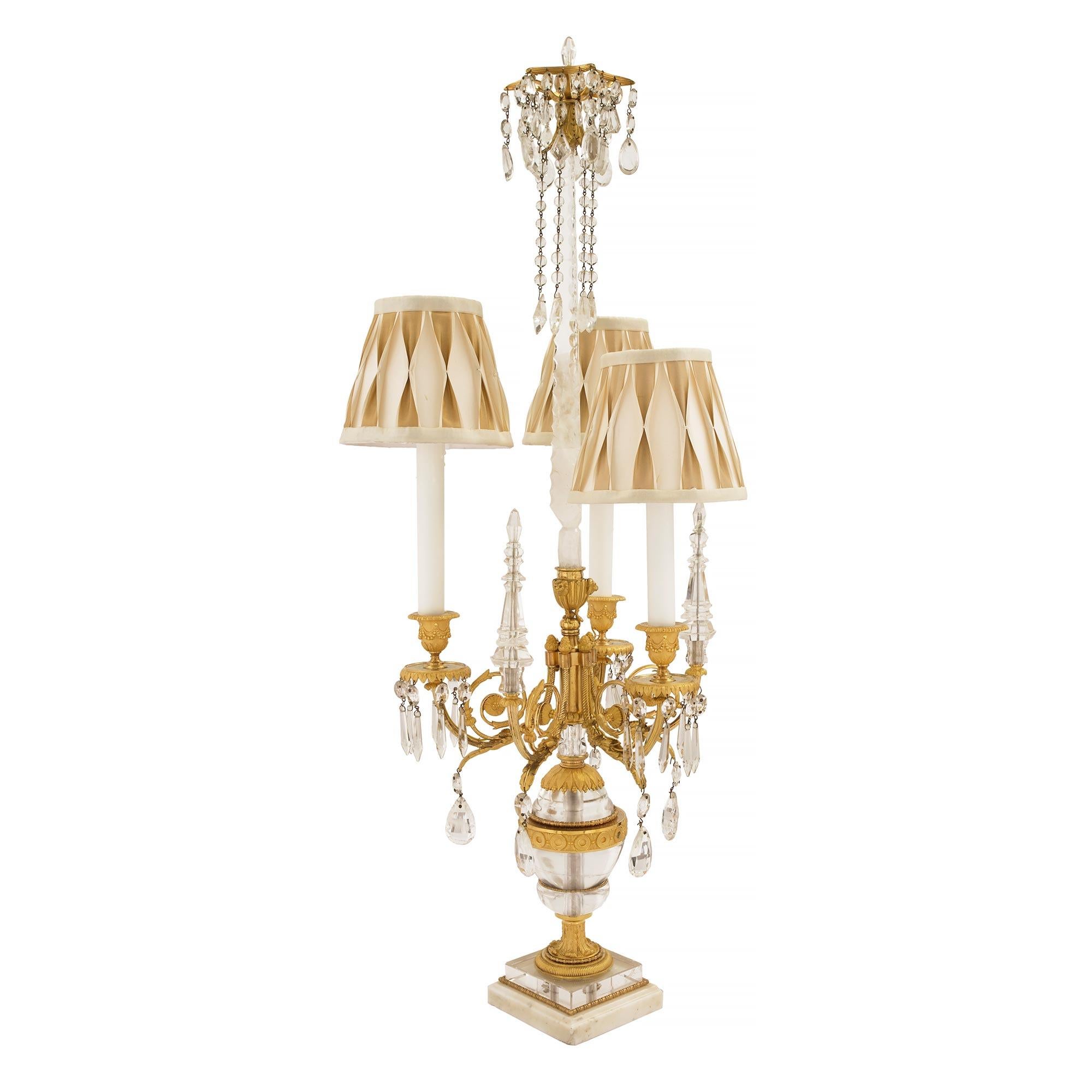 A sensational pair of French 19th century Louis XVI st. rock crystal, Baccarat crystal and ormolu candelabra lamps. Each lamp is raised by a square white Carrara marble base with a mottled border and a rock crystal support framed within a charming