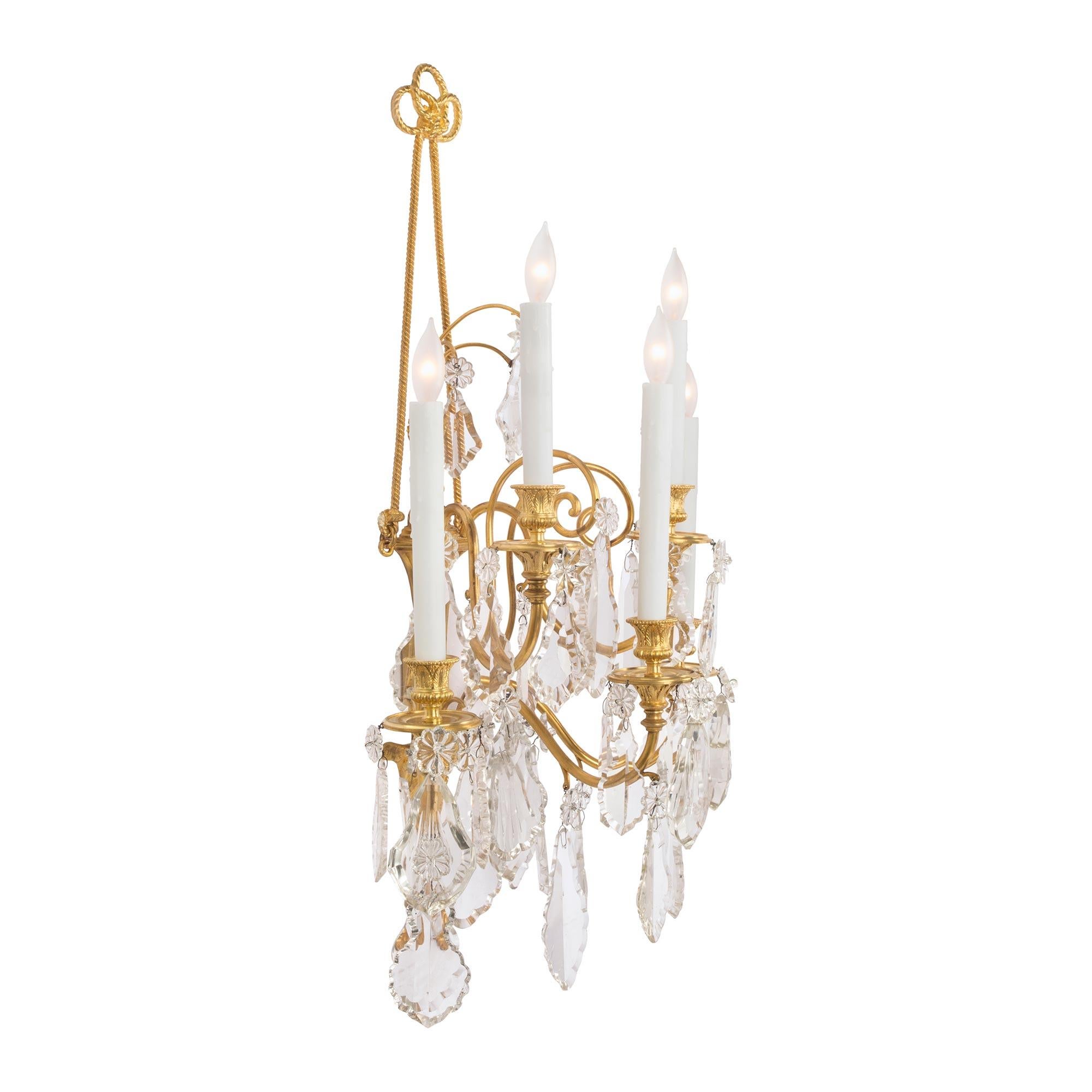 A stunning and large scale pair of French 19th century Louis XVI st. ormolu and Baccarat crystal five arm sconces. Each sconce is centered by beautiful and richly chased berried and foliate movements with finely etched designs below a large acanthus