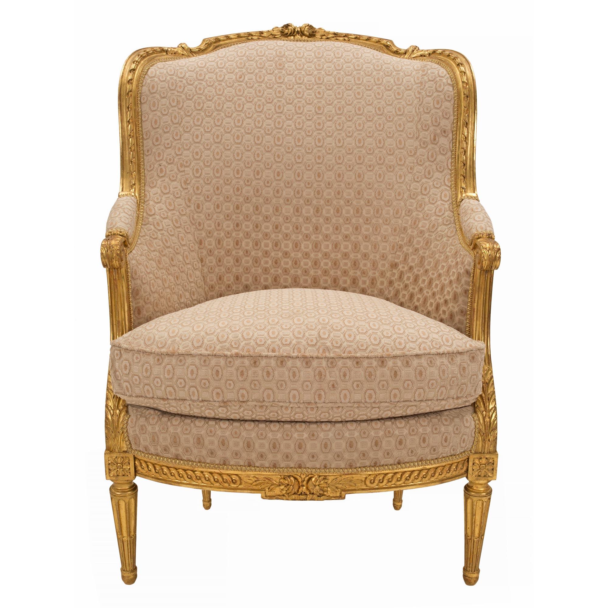 A striking pair of French 19th century Louis XVI st. giltwood Bergères à Oreilles. Each armchair is raised by circular tapered fluted legs below fine block rosettes. Extending along the frieze are impressive and wonderfully carved interlocking