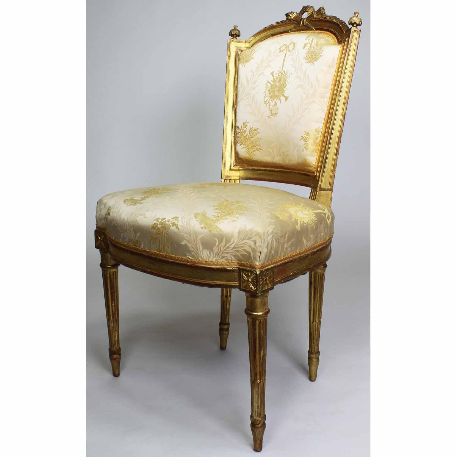 Pair of French 19th century Louis XVI style giltwood carved Boudoir side chairs. The low giltwood carved frames with a padded tapered backrest crowned with carved crossed flaming torches and ribbon, flanked by a pair of corner finials, raised four