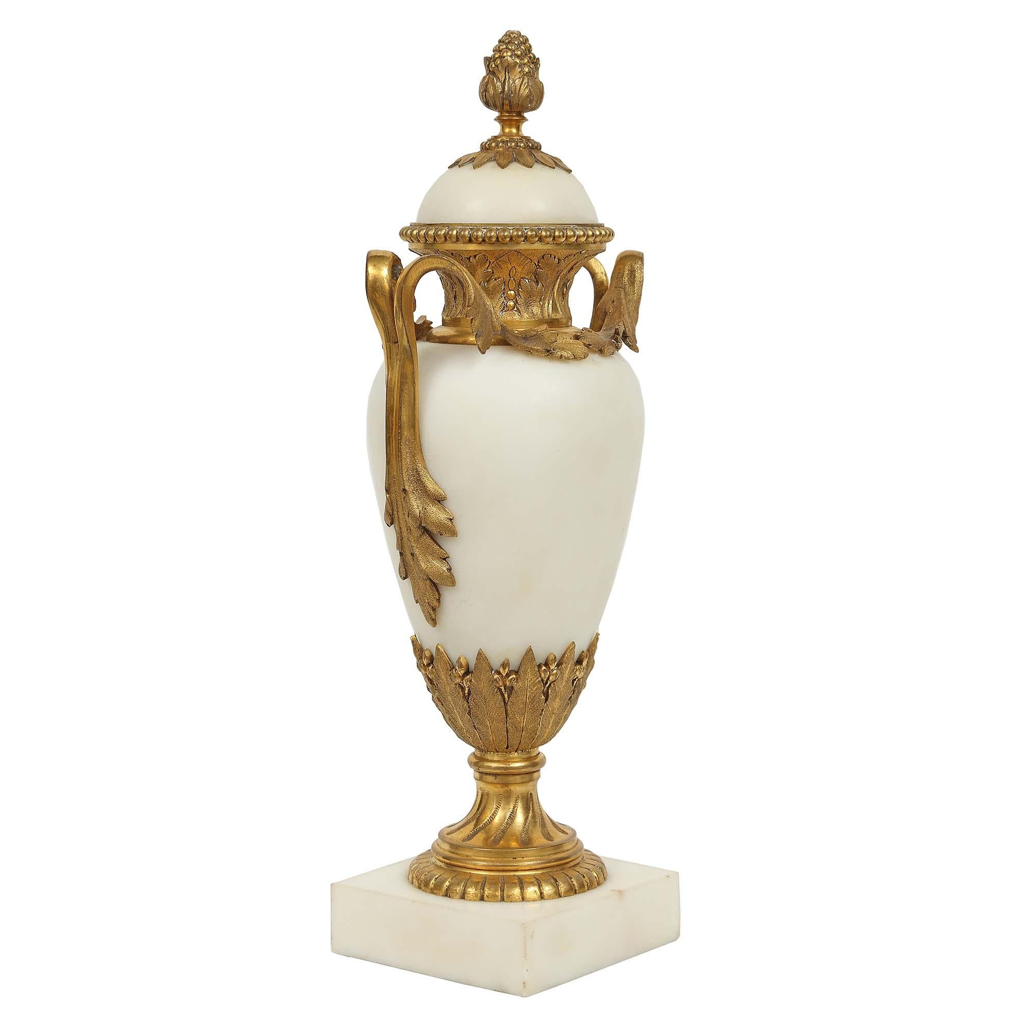 Une très belle paire de cassolettes françaises du 19ème siècle, de style Louis XVI, en marbre blanc de Carrare et bronze doré, avec toutes les dorures d'origine. La paire est surélevée par une épaisse base en marbre de forme carrée. Au-dessus se
