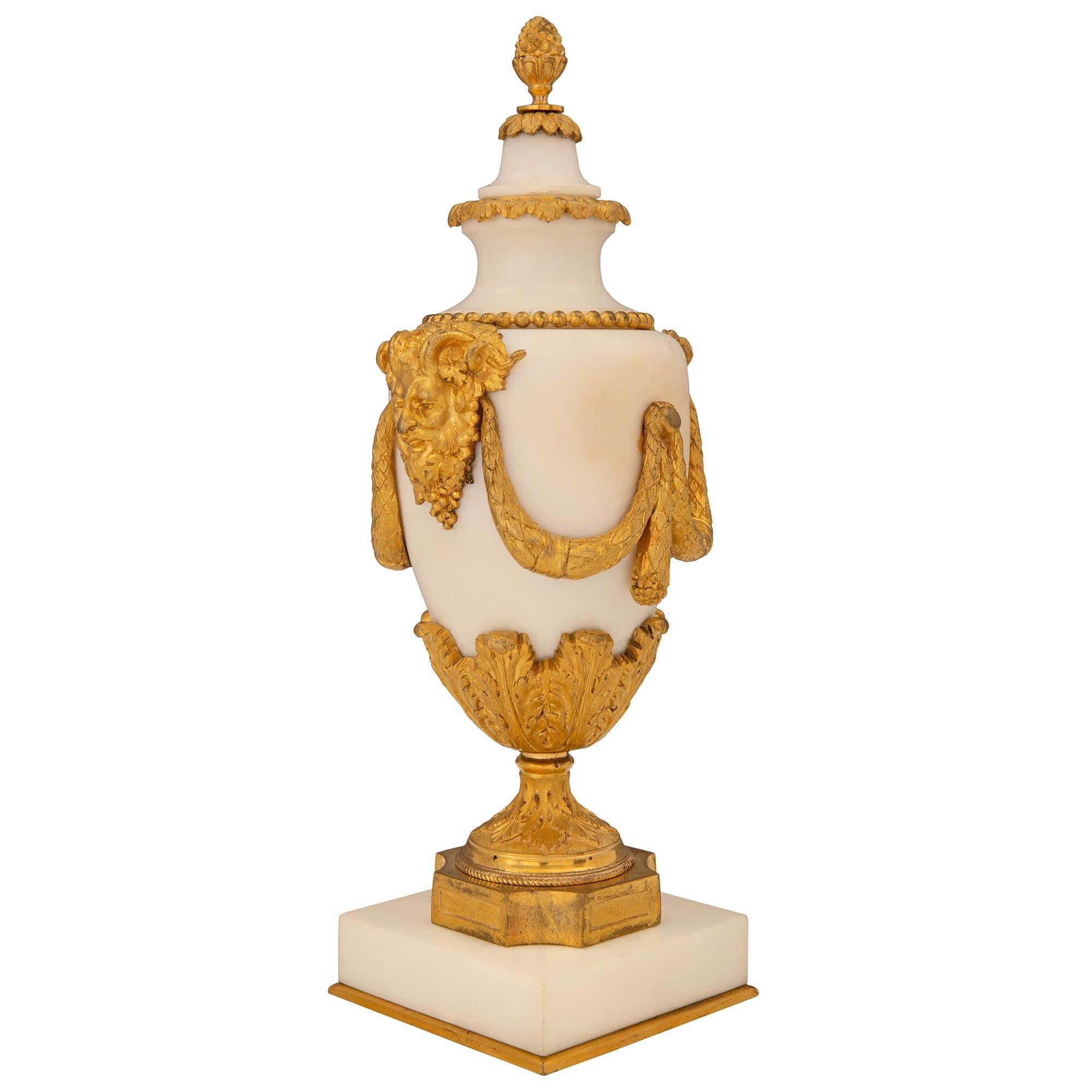 An elegant pair of French 19th century Louis XVI st. white Carrara marble and ormolu lidded cassolette urns. Each cassolette is raised by a square white Carrara marble base with a fine bottom ormolu fillet. The ormolu socle shaped pedestal supports