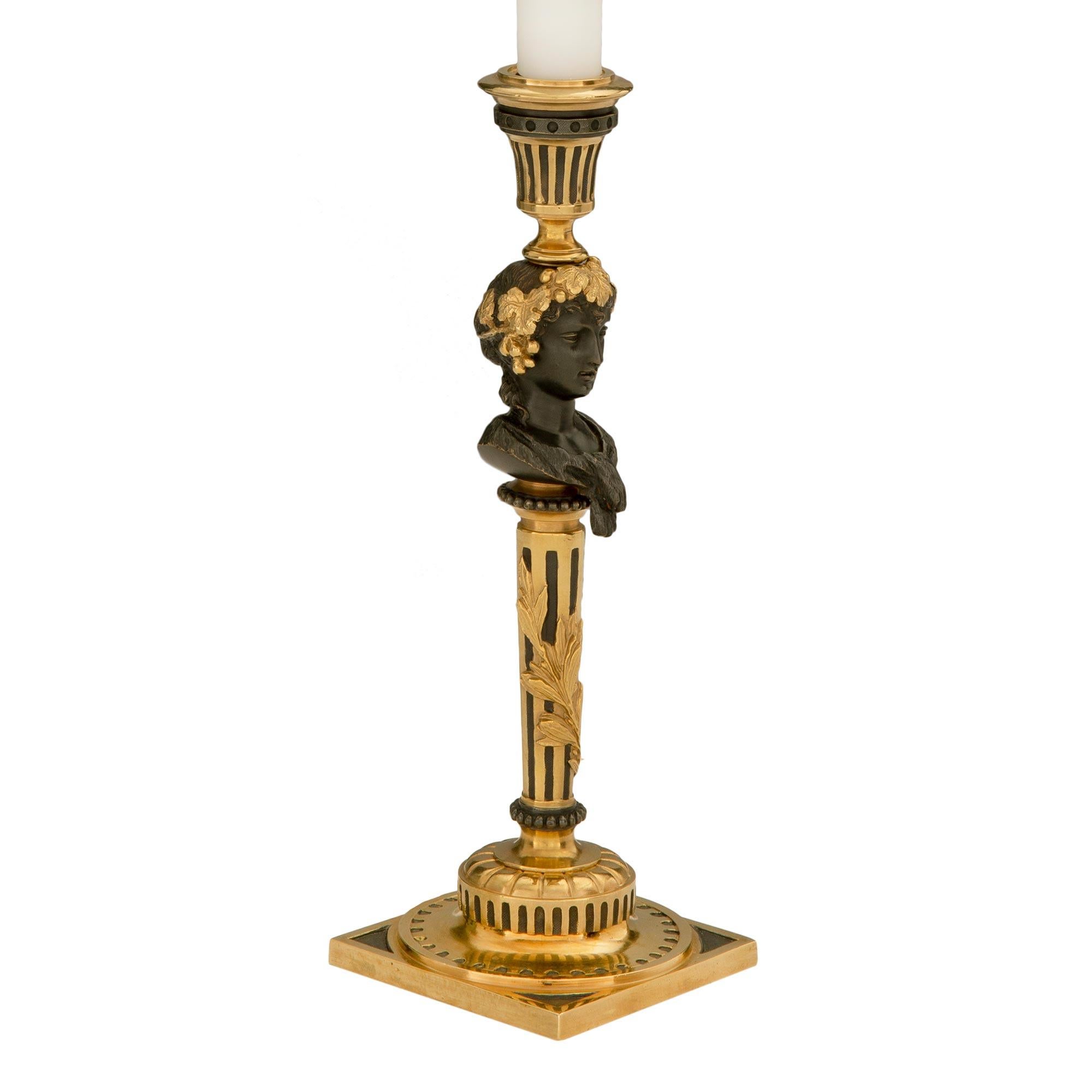A most elegant pair of French 19th century Louis XVI st. ormolu and patinated bronze electrified candlestick lamps. Each lamp is raised by a square base in a unique and most decorative ormolu and patinated bronze design. The circular tapered