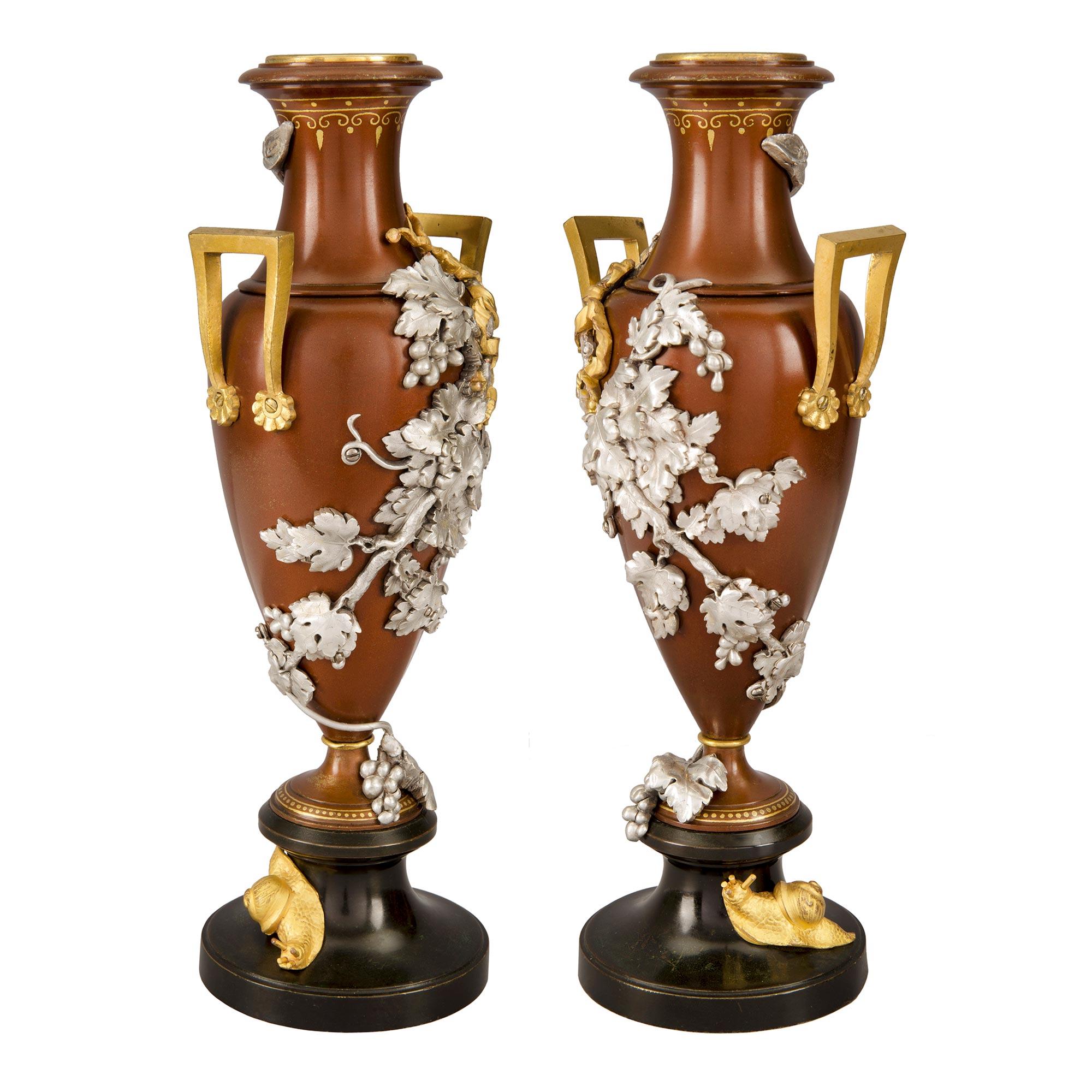 A stunning pair of French 19th century Louis XVI st. silvered bronze, ormolu and two toned patinated bronze urns. Each lovely urn is raised by a patinated bronze socle pedestal with a charming and richly chased ormolu snail at the side. The elegant