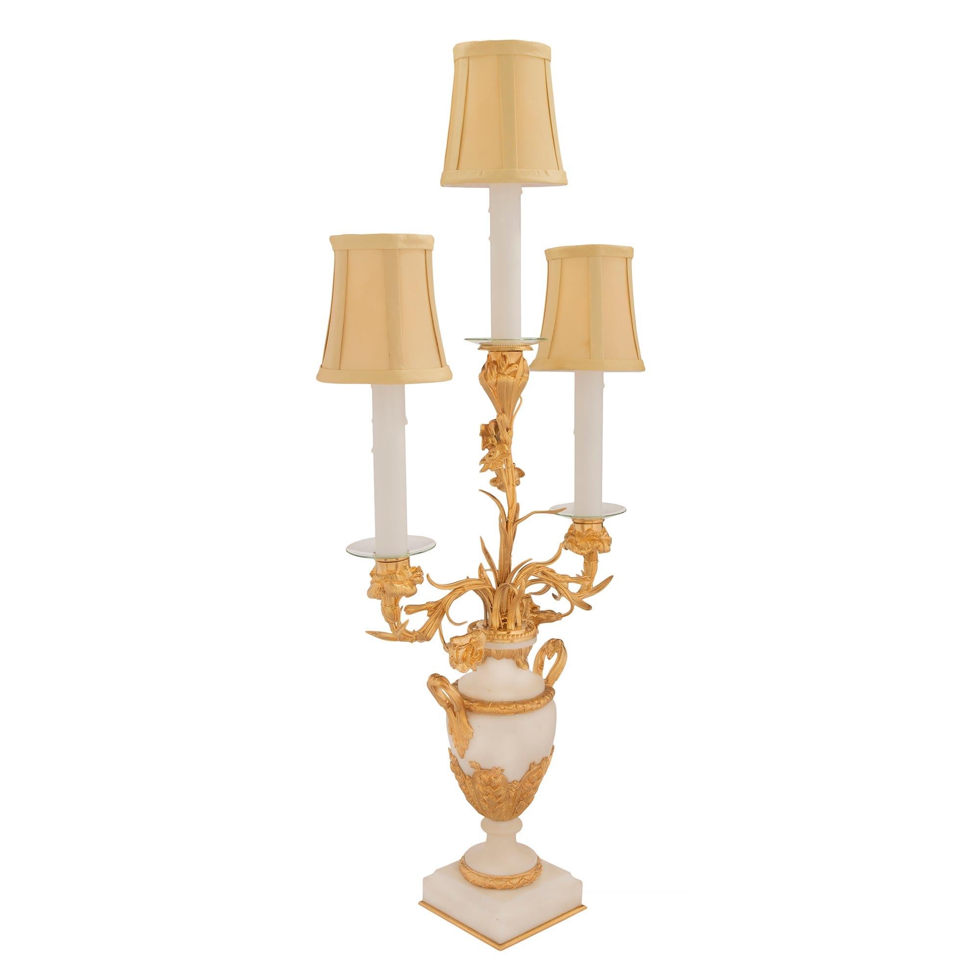 Une élégante paire de lampes candélabres à trois bras de style Louis XVI du 19ème siècle, en bronze doré et marbre blanc de Carrare. Chaque lampe est surélevée par de fins pieds à boule en bronze doré sous une base carrée en marbre blanc de Carrare