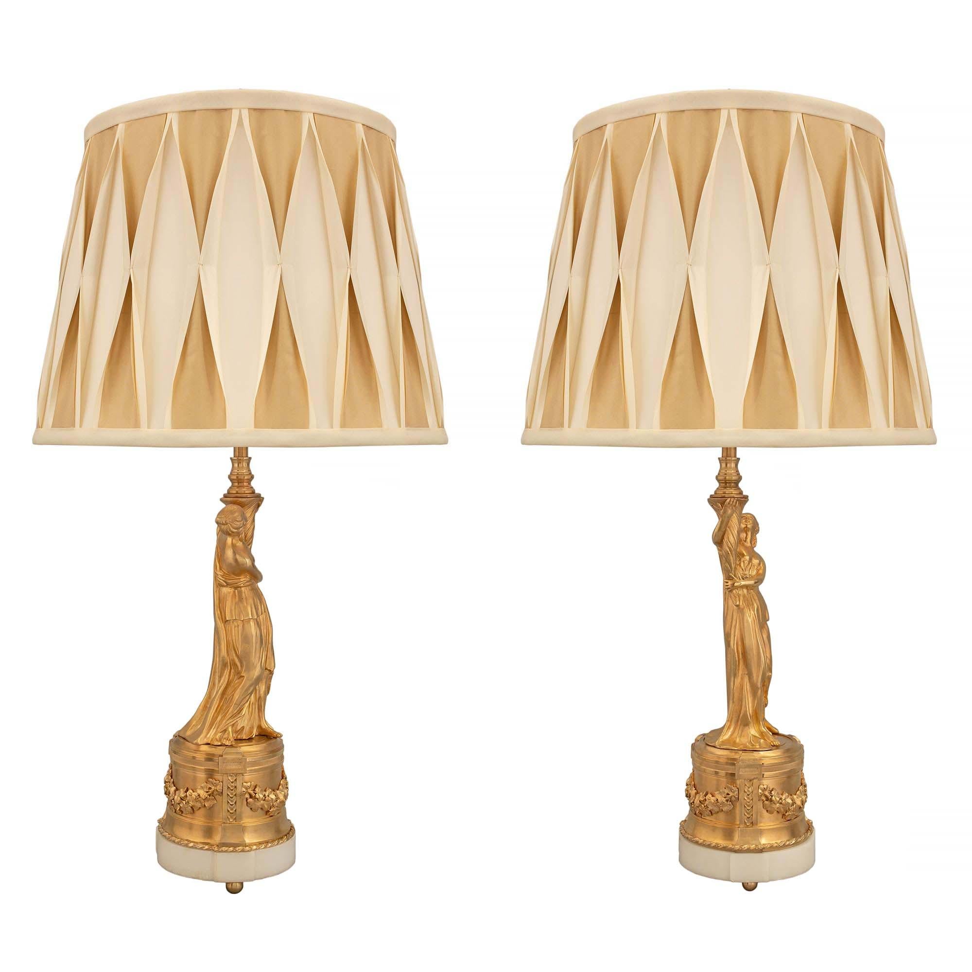 A very elegant pair of French 19th century Louis XVI st. ormolu and white Carrara marble statues mounted into lamps. Each lamp is raised by bun ormolu supports below a circular white Carrara marble base. Above the base is a circular ormolu column