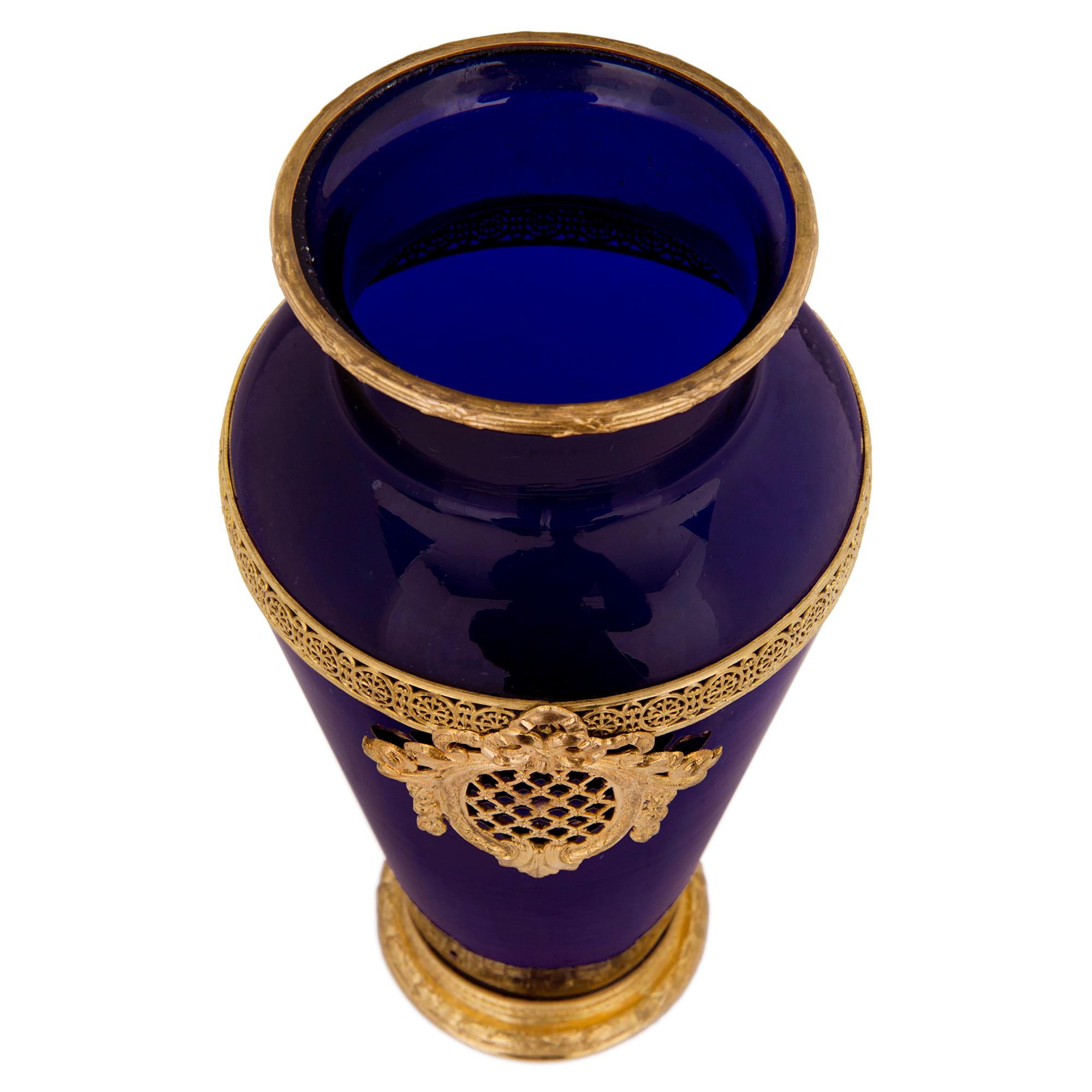 An elegant pair of French 19th century Louis XVI st. ormolu and cobalt blue glass vases. Each vase is raised by a lovely ormolu base with a fine berried laurel band and a lovely interlocking guilloche design. The baluster shaped cobalt blue glass