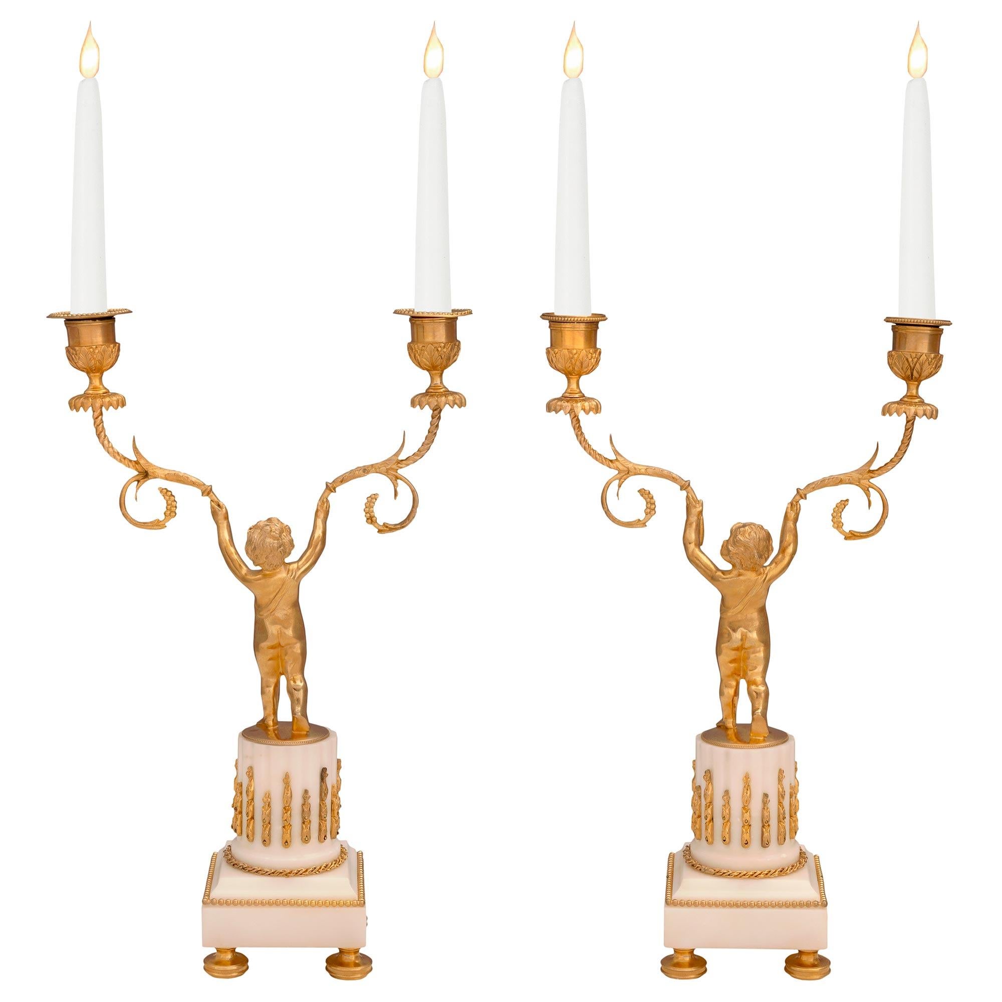 An elegant true pair of French 19th century Louis XVI st. ormolu and white Carrara marble candelabras. Each candelabras is raised by fine mottled bun shaped feet below the square white Carrara marble base. The bases display charming intertwined