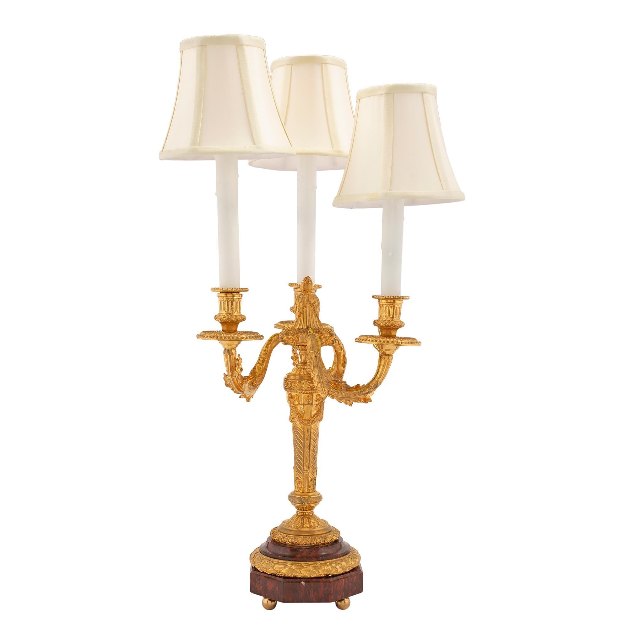 An elegant and high quality pair of French 19th century Louis XVI st. ormolu and Rouge Griotte marble three arm electrified candelabra lamps. Each lamp is raised by fine ormolu ball feet below an octagonal Rouge Griotte marble base with a mottled