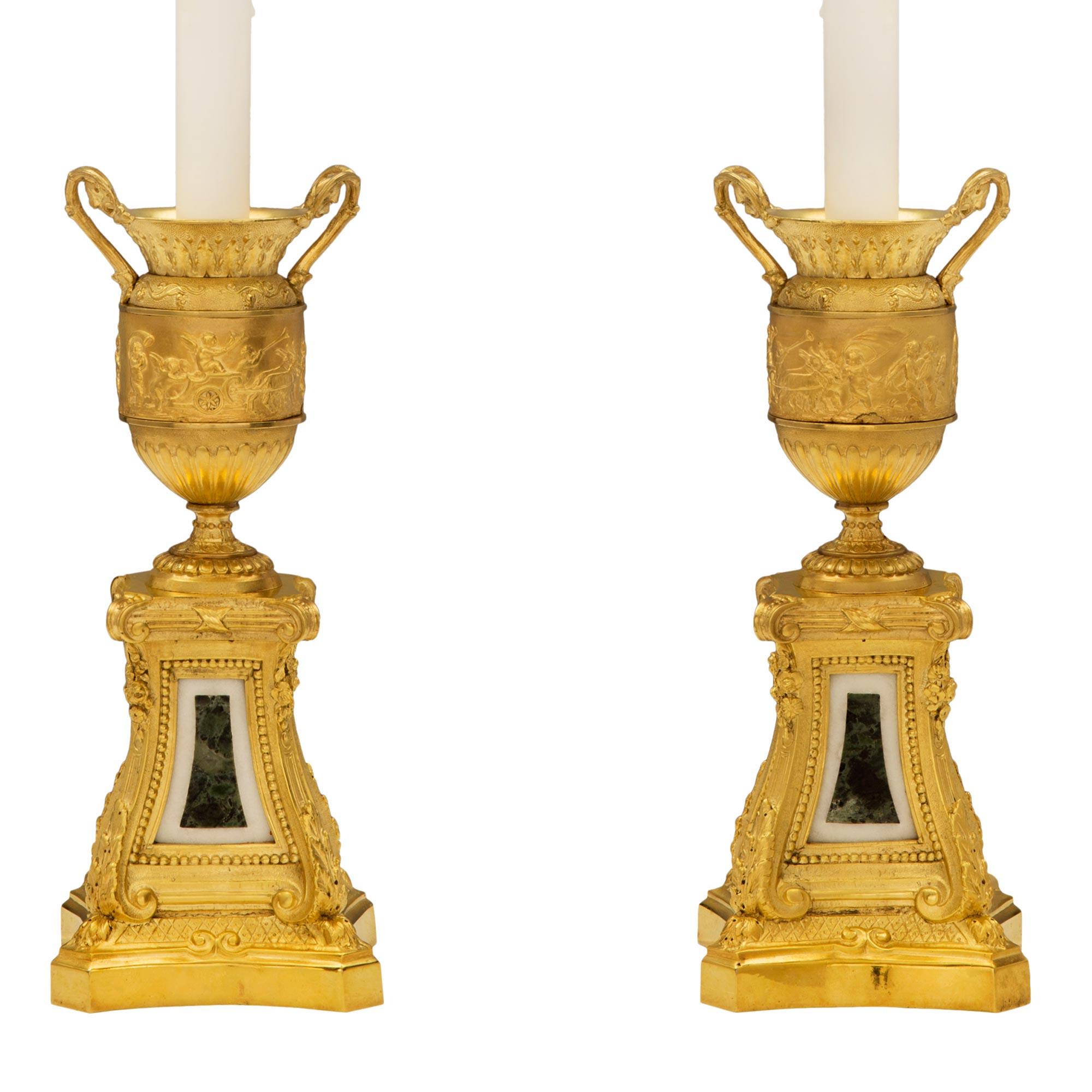 An exceptional pair of French 19th century Louis XVI st. ormolu, white Carrara marble and Vert de Patricia marble lamps after a model by Clodion. Each lamp is raised by a square base with concave sides and mottled border. The central supports