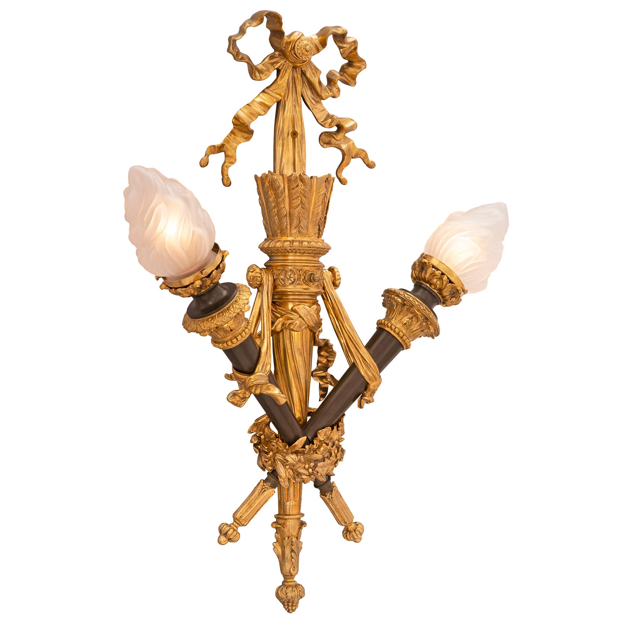 A superb pair of French 19th century Louis XVI style ormolu and patinated bronze sconces. Each two arm sconce is centered by a beautiful bottom acorn finial amidst large acanthus leaves. At the centers are crossed torches of the eternal flames each