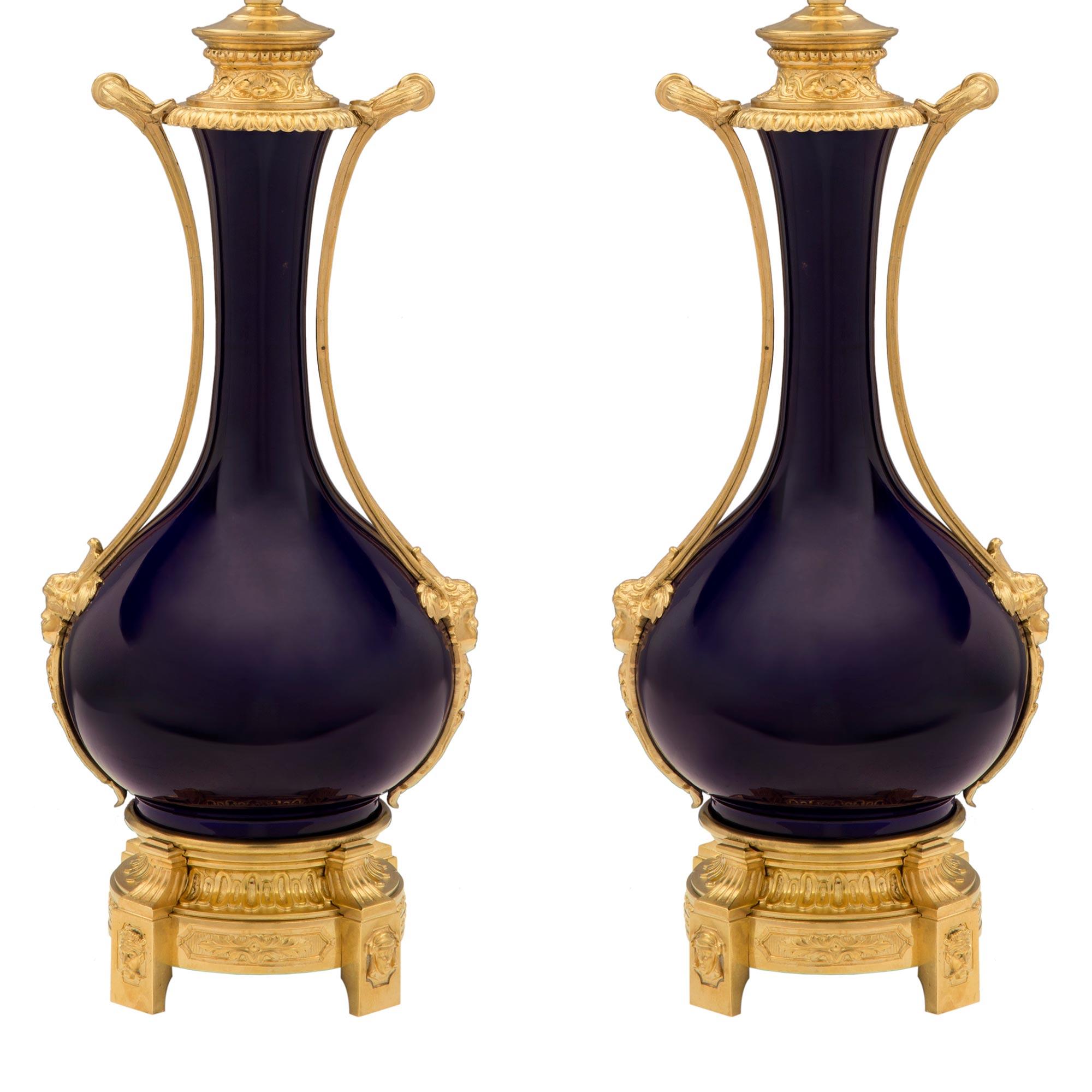 An elegant pair of French 19th century Louis XVI st. ormolu and cobalt blue Sèvres porcelain lamps. Each lamp is raised by fine feet with lovely richly chased faces centering recessed floral designs. Above the fluted circular mottled supports are