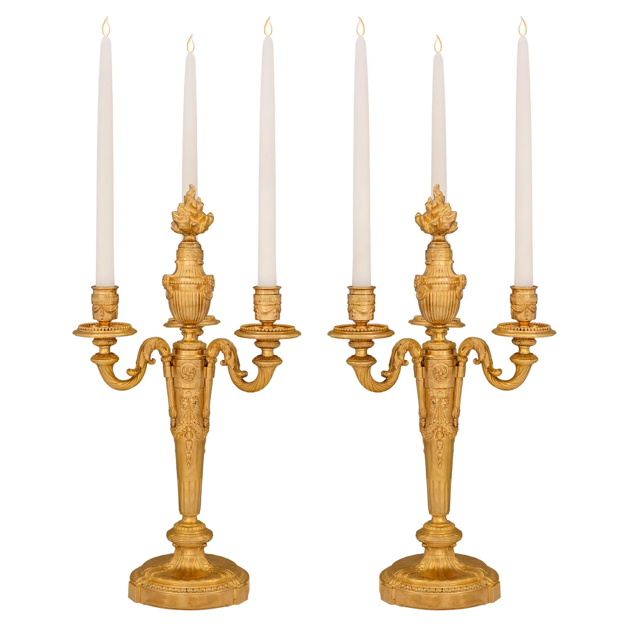 A most elegant pair of French 19th century Louis XVI st. ormolu candelabras. Each three arm candelabra is raised by a Fine circular base with a detailed Coeur de Rai wrap around band and acanthus leaves. The tapered central supports display richly